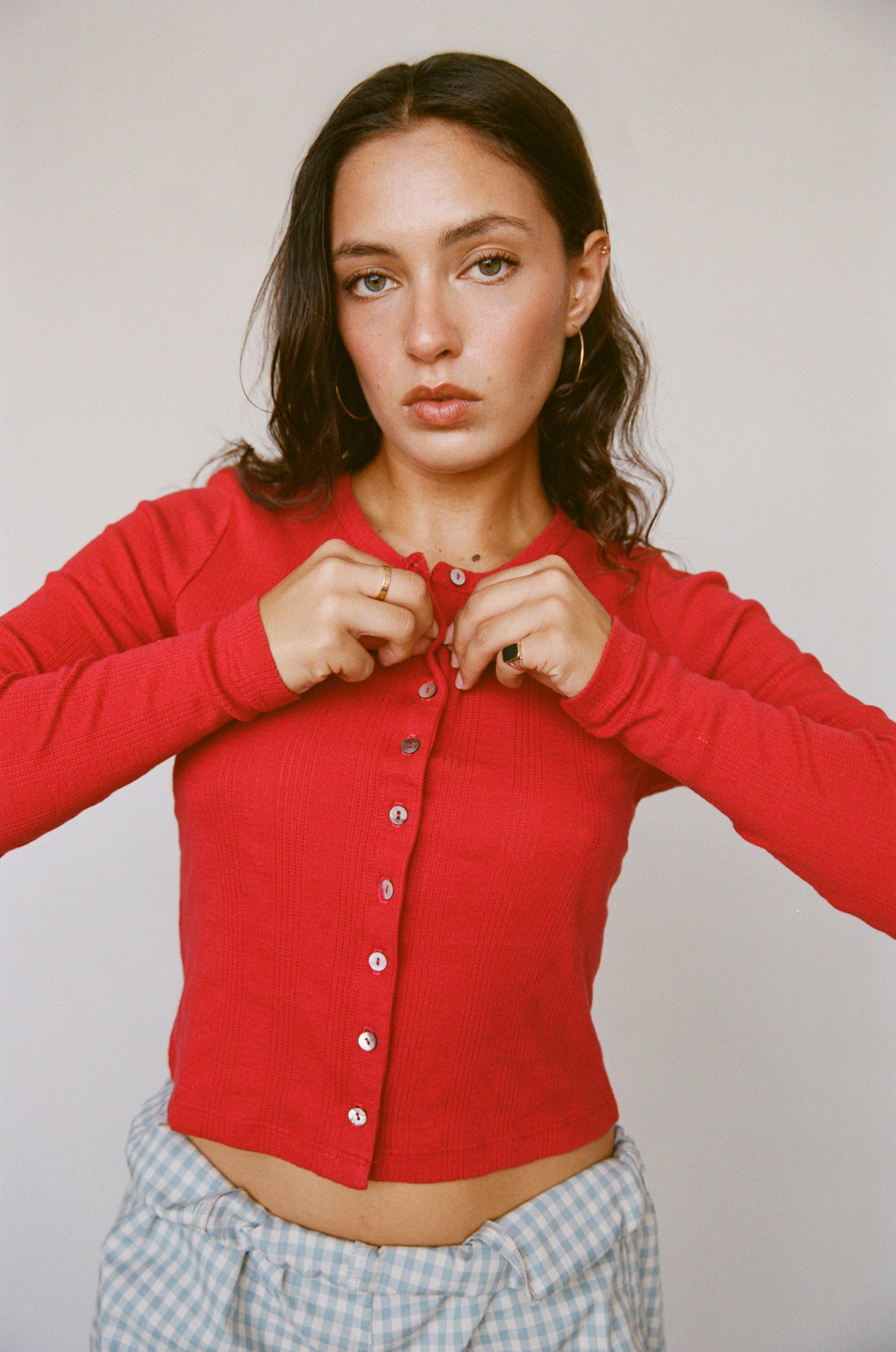 Red ribbed cardigan with white buttons, long sleeves, and cropped fit worn with blue gingham pants