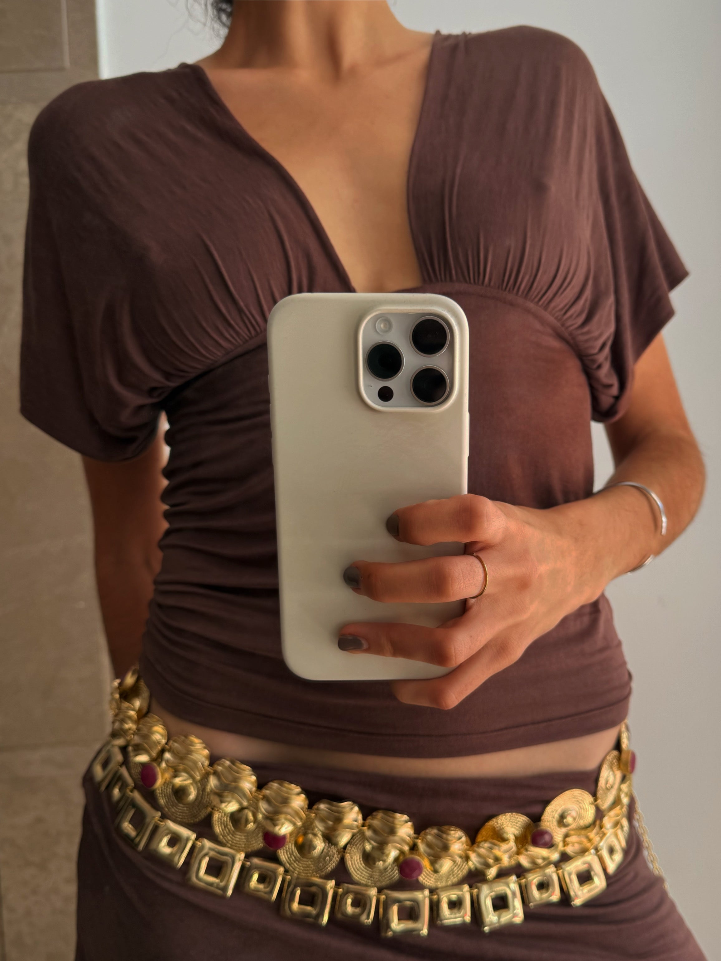 Woman wearing brown ruched top with plunging neckline and ornate gold statement belt with geometric details