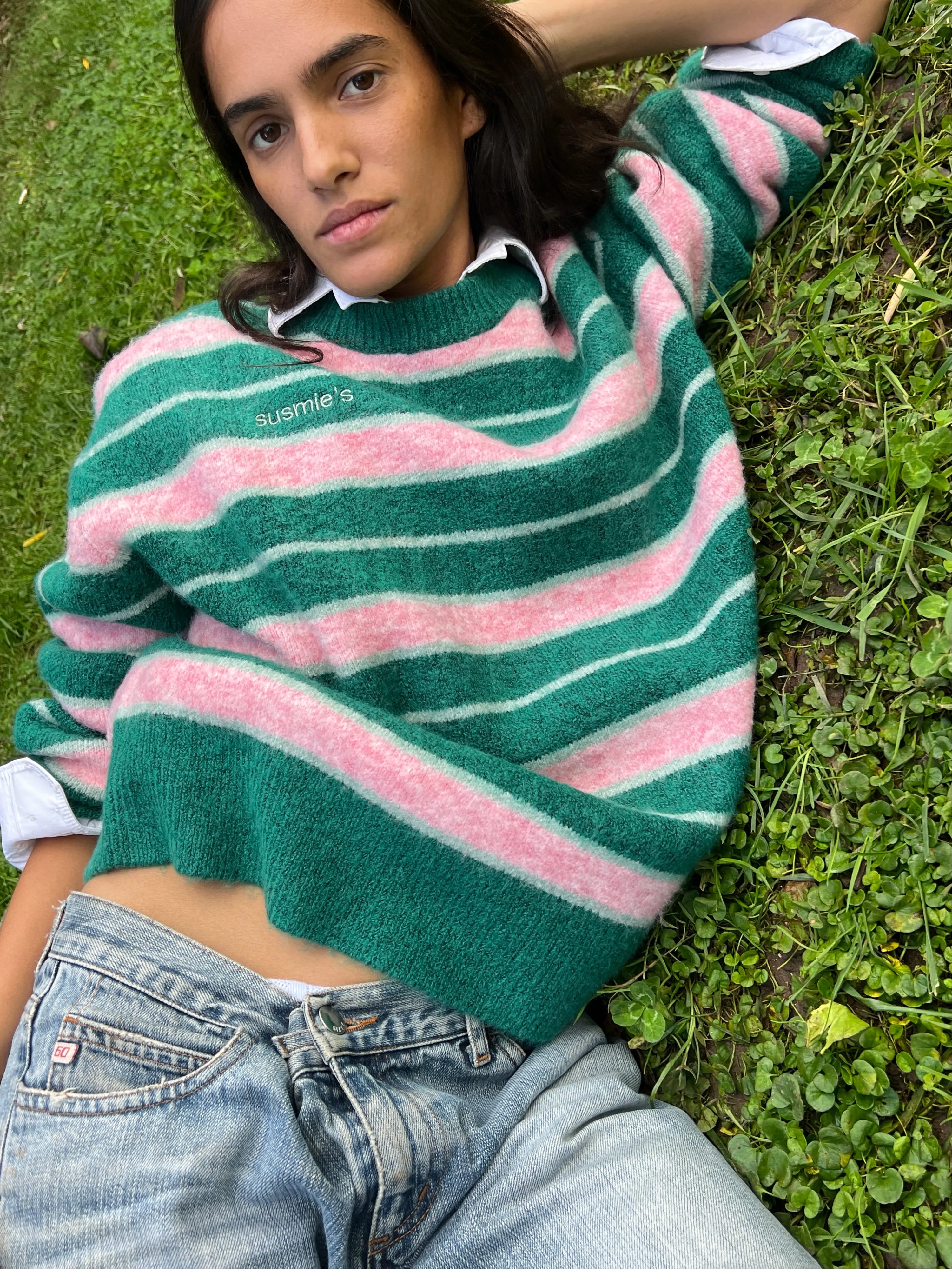 Green and pink striped knit sweater with white collar detail, worn casually while lying on grass