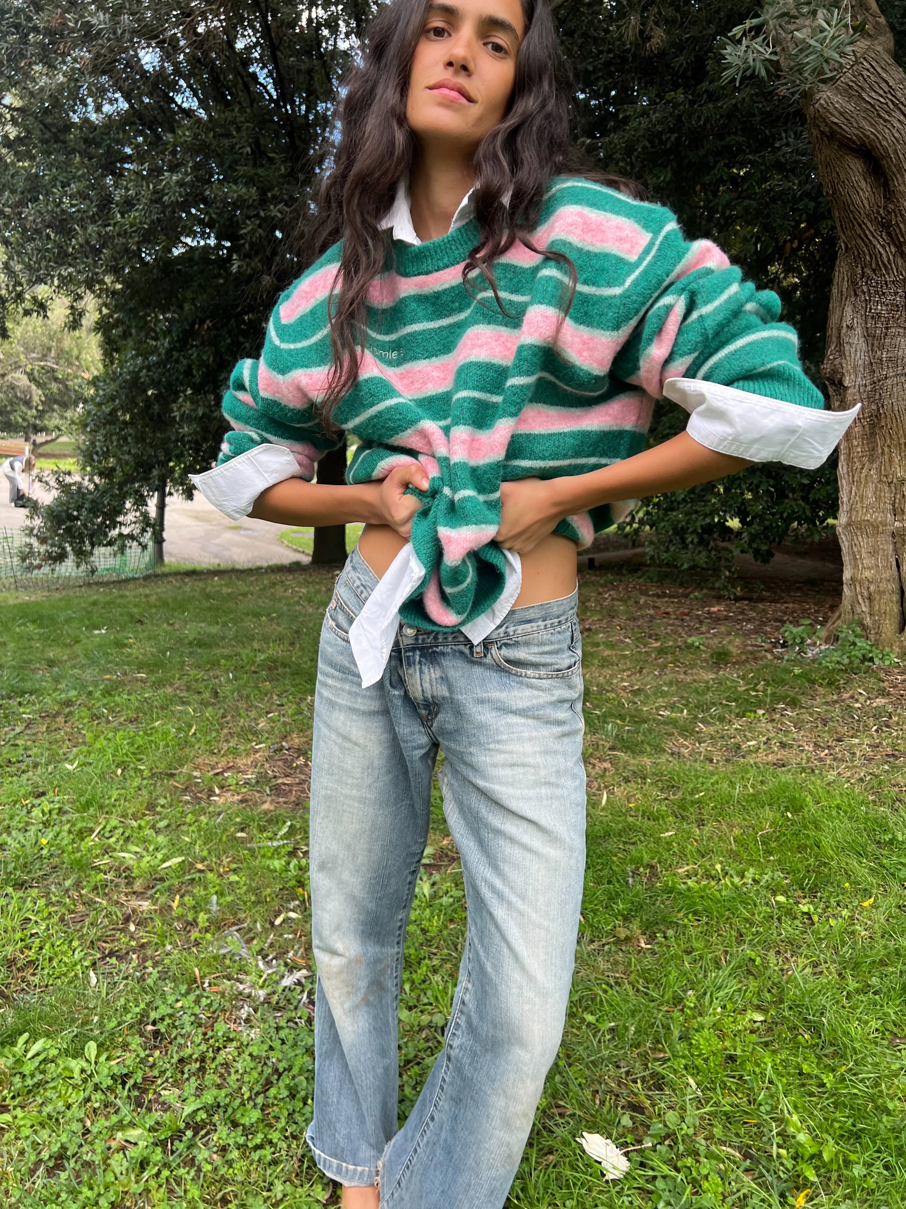 Green and pink striped oversized knit sweater layered over white collared shirt with light wash jeans