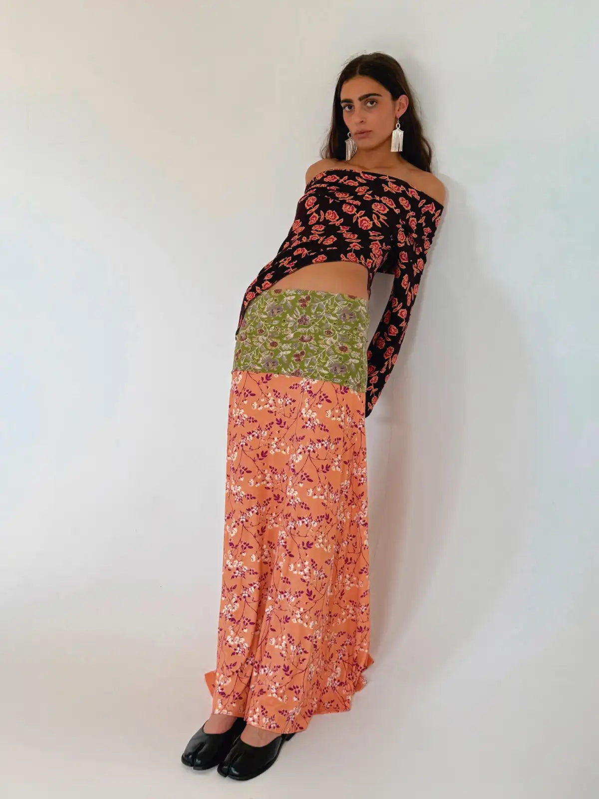 Woman wearing off-shoulder black floral top and mixed floral print maxi skirt in coral, pink, and green tones with black shoes