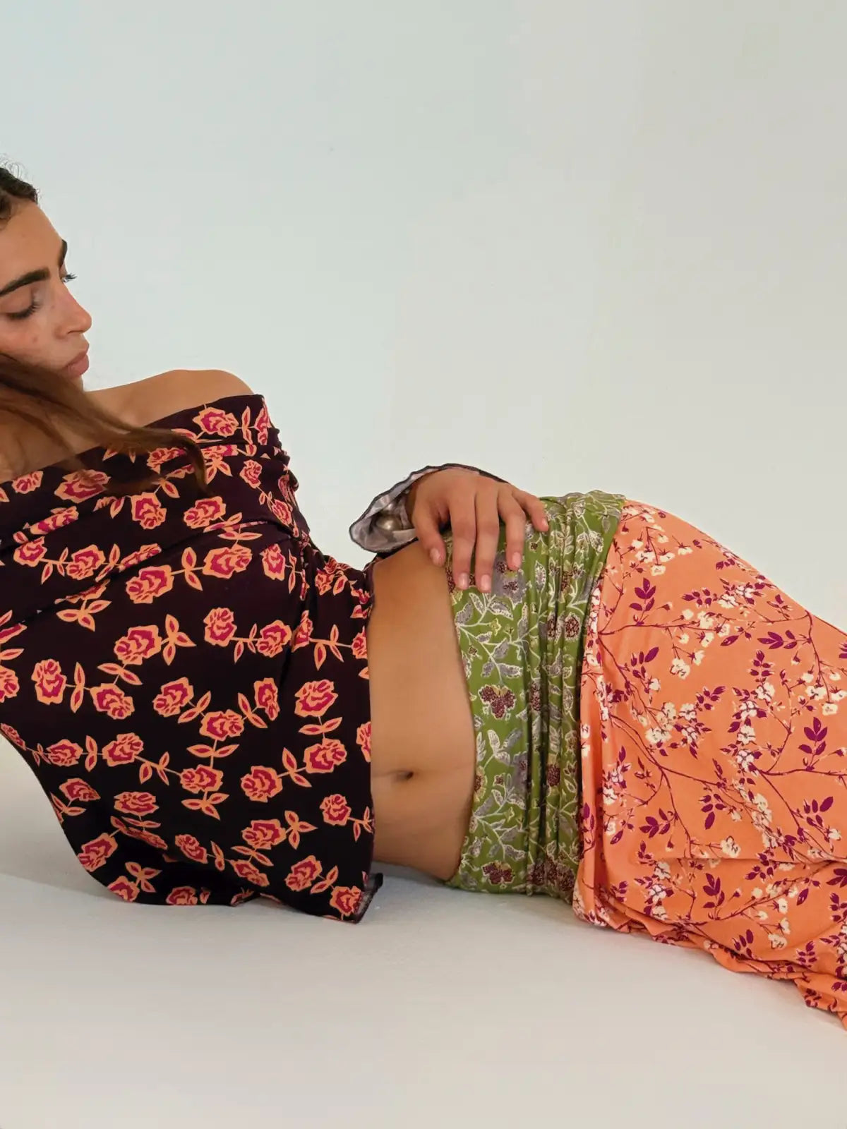 Person wearing floral print skirts in black with red roses, green botanical print, and orange with purple florals