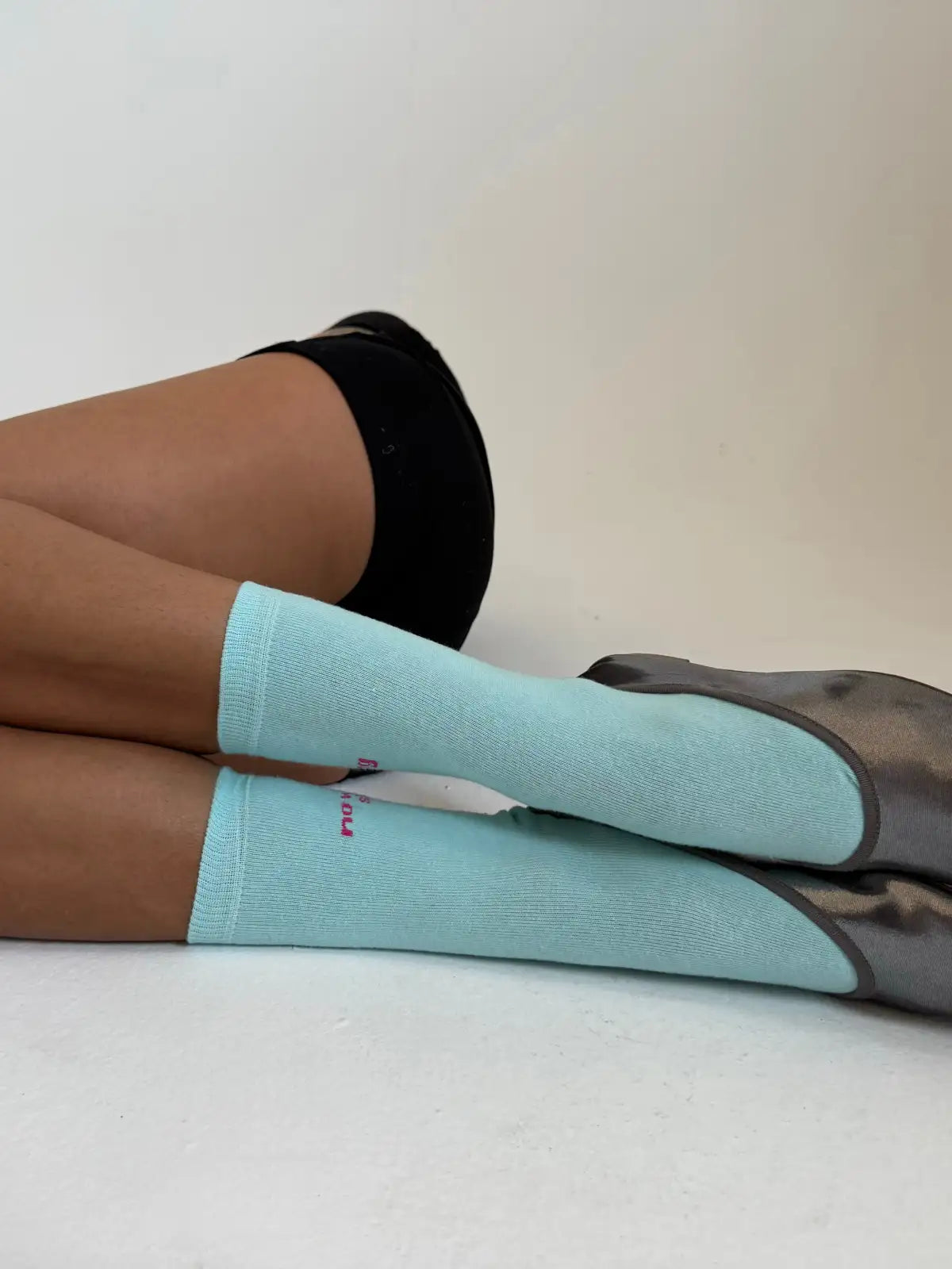 Light blue ribbed socks with black soles worn with black shorts, legs elevated against white background
