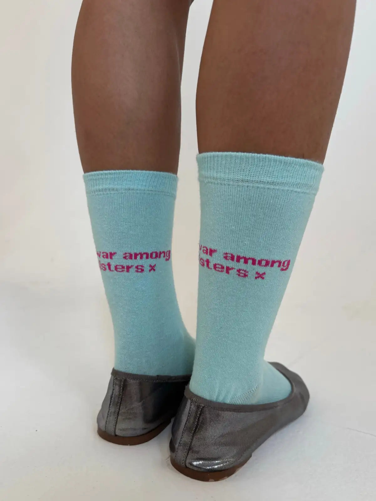 Light blue socks with pink text reading "war among sisters" worn with brown pantyhose and black flats