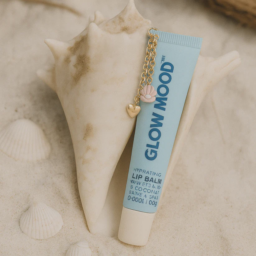Lip balm tube with 'Glow Mood' branding on a sandy background with shells.