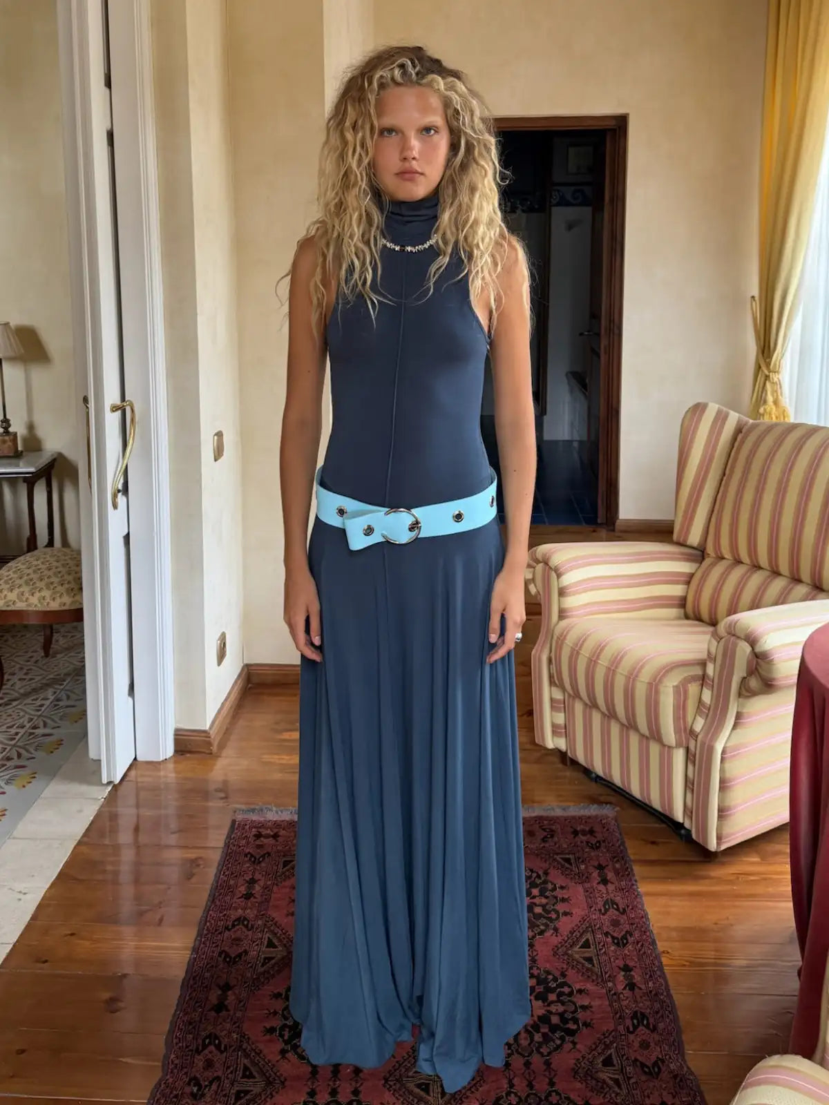 Navy sleeveless turtleneck maxi dress with flowing skirt and light blue belt featuring circular buckle detail