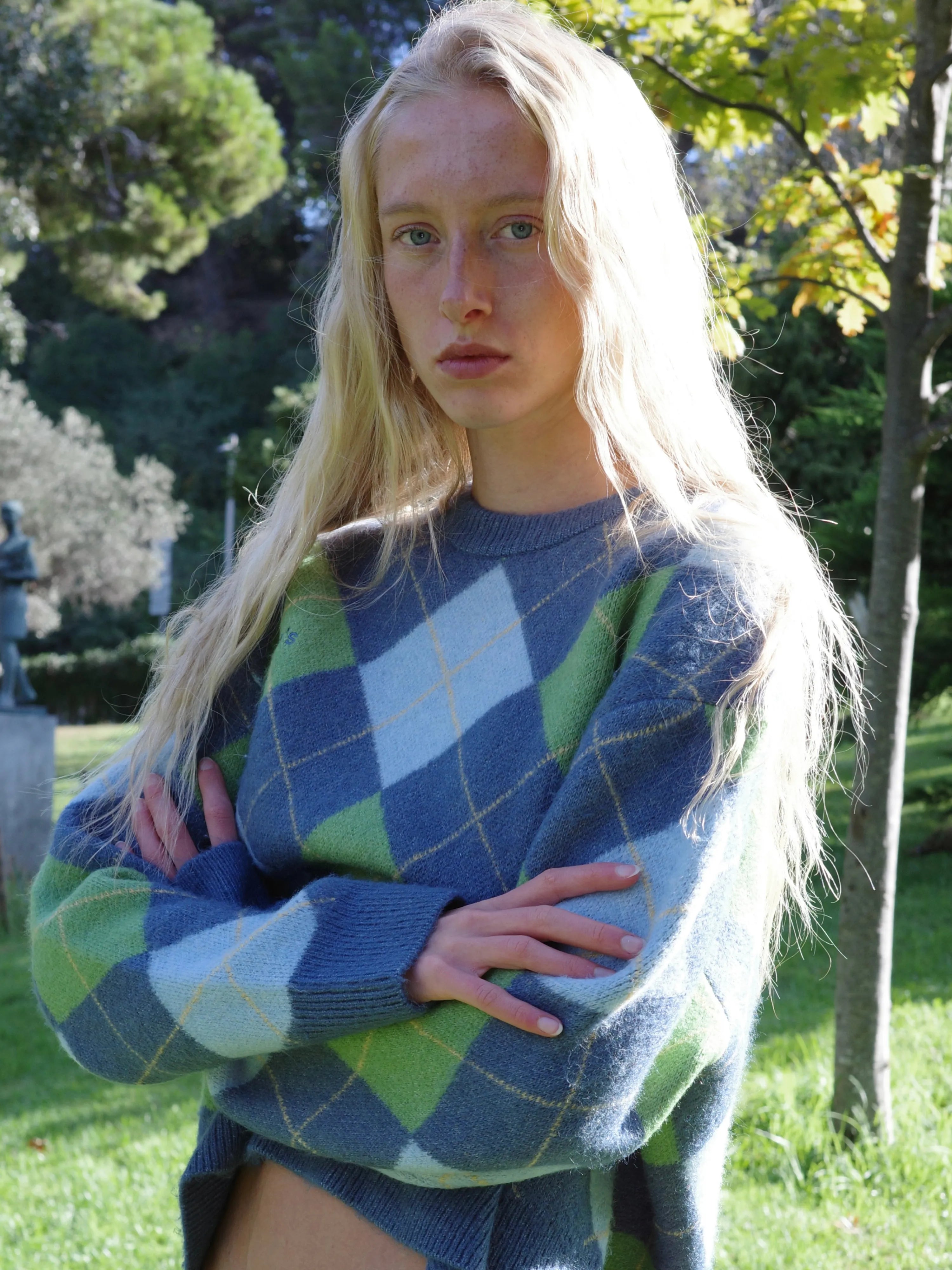 Blue and green argyle knit sweater with long blonde hair model in outdoor park setting
