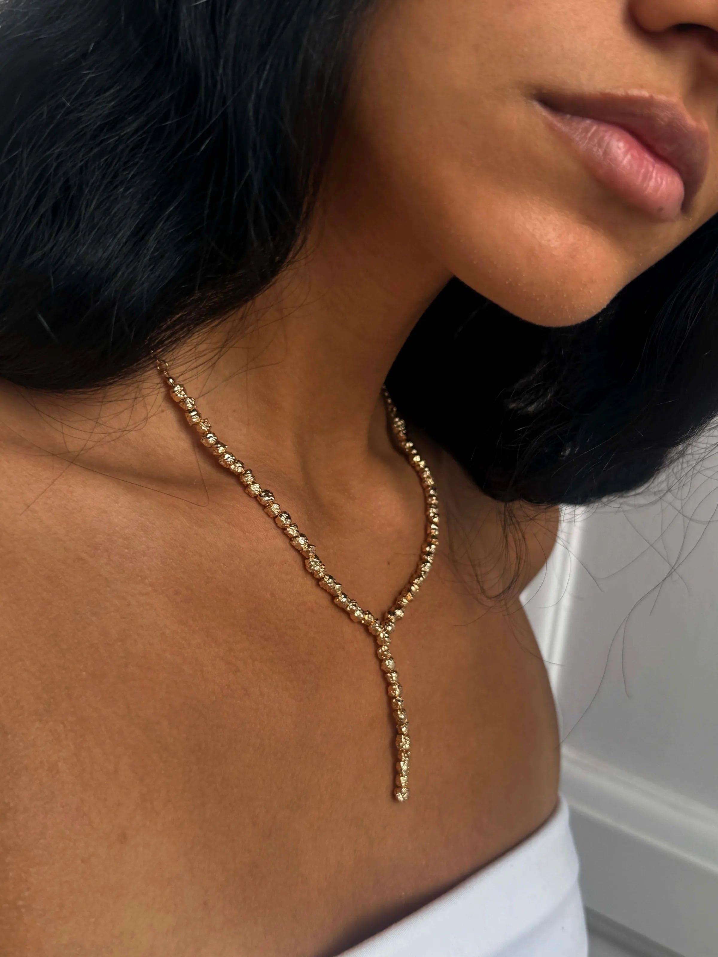Gold beaded Y-shaped lariat necklace with drop pendant worn on neck against white top