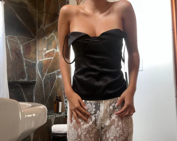 Woman wearing a black strapless top and lace pants in a room with stone walls.