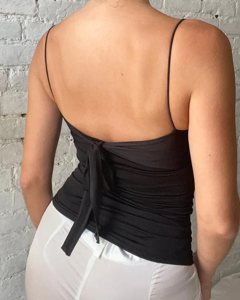 Person wearing a black tank top with thin straps against a gray brick wall.
