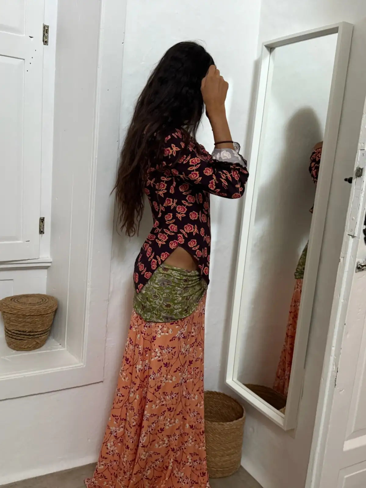 Woman wearing black floral top and colorblock maxi skirt with green and peach floral tiers, viewed from back