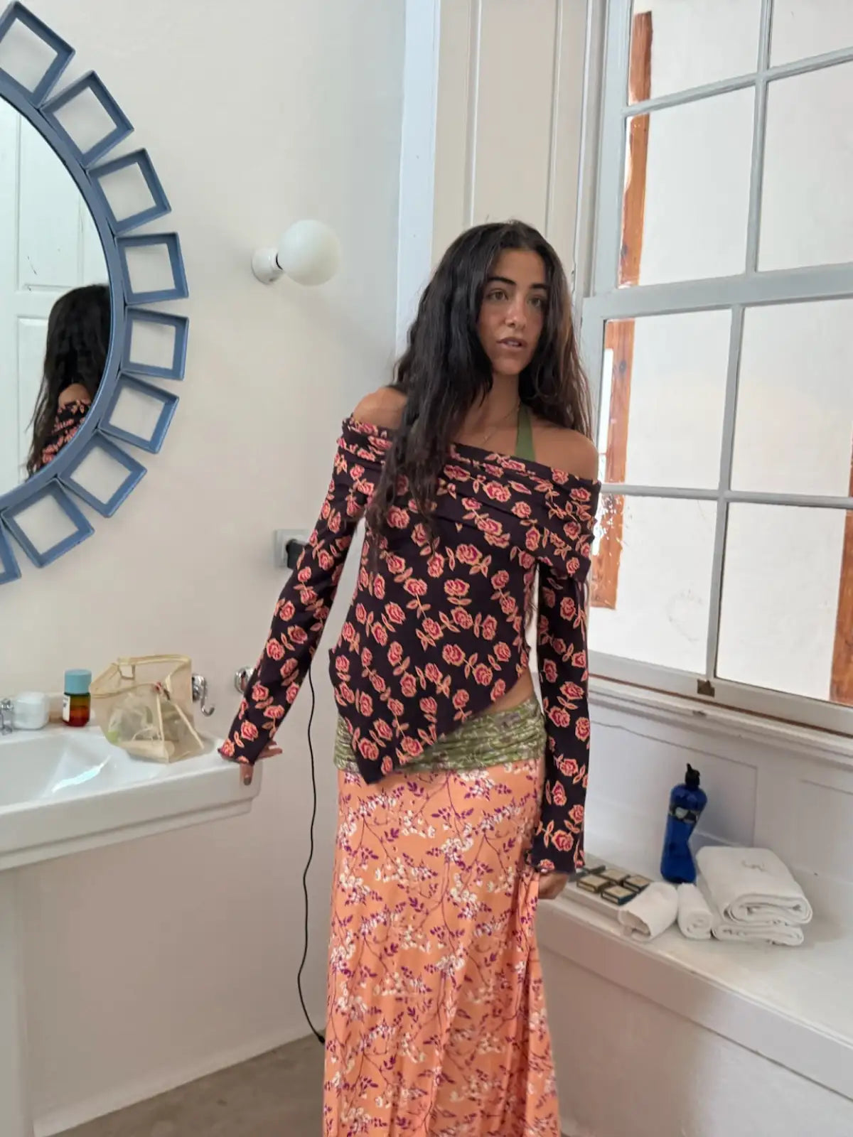 Woman wearing off-shoulder black floral top with long sleeves and peach floral maxi skirt with green velvet waistband