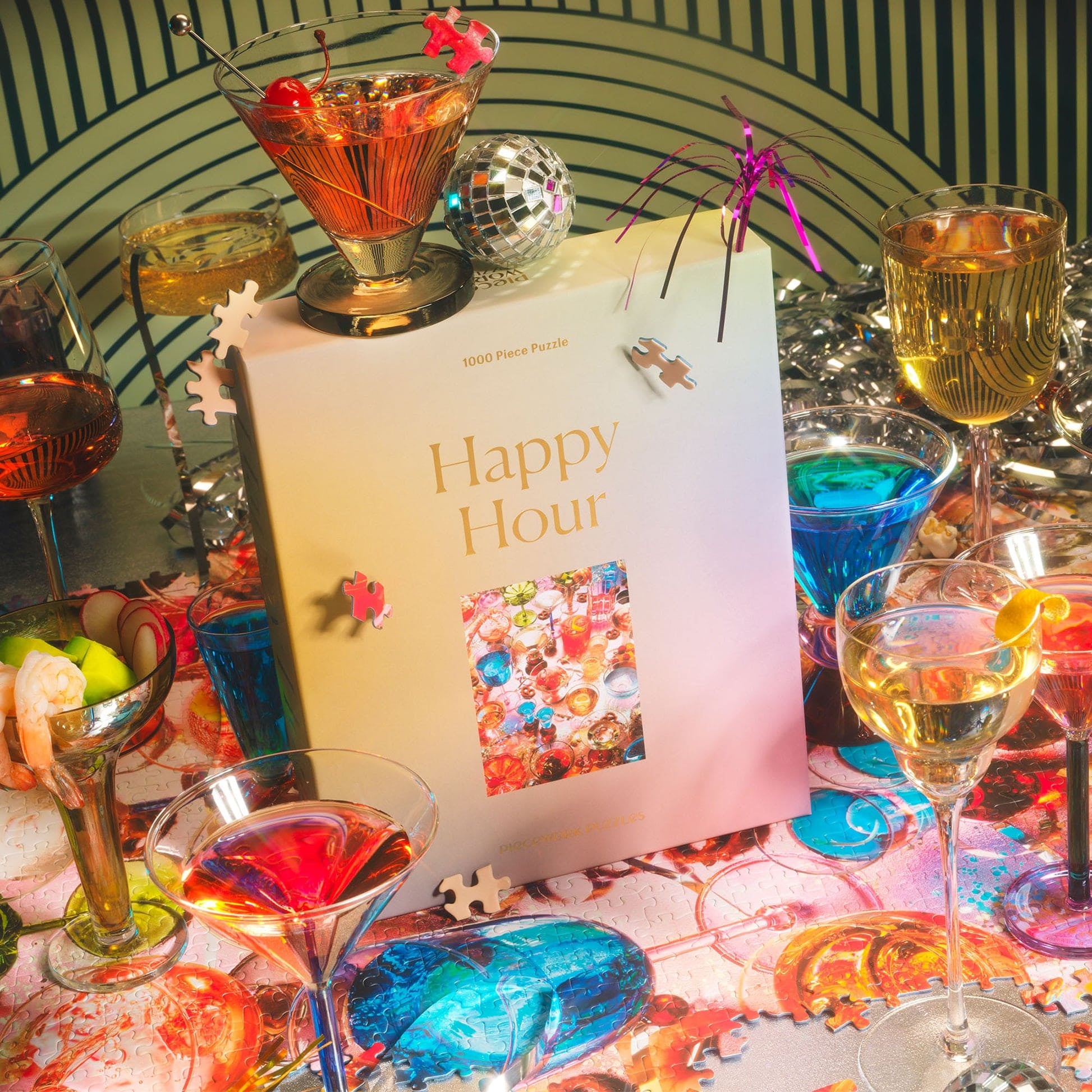Colorful Happy Hour jigsaw puzzle box surrounded by vibrant cocktail glasses, disco ball, and festive party decorations