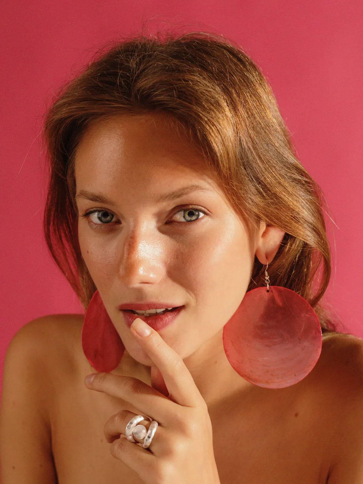 Large circular red resin statement earrings with silver hardware, shown on model against pink background