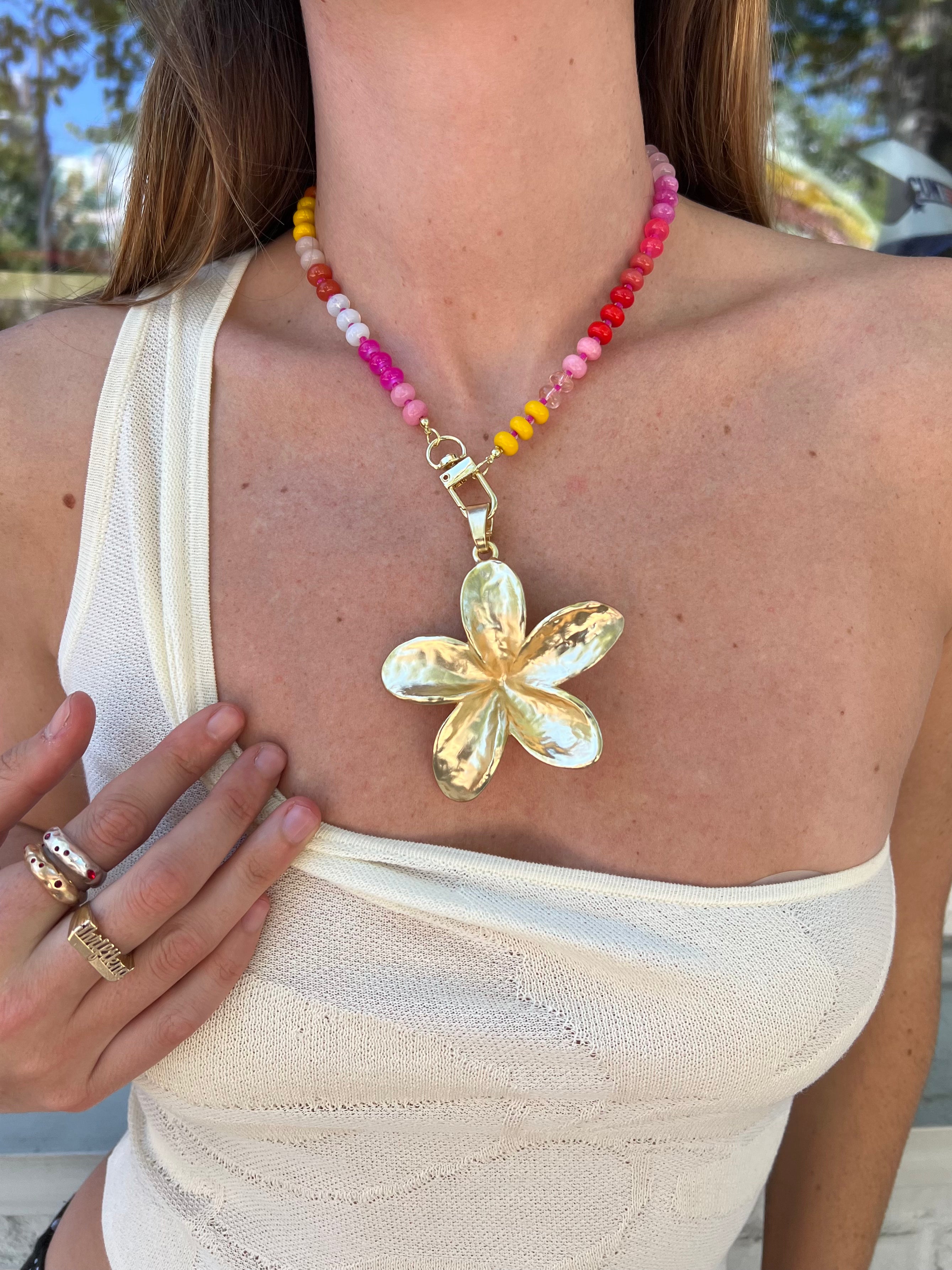 Colorful beaded necklace with gold flower pendant and toggle clasp, featuring pink, red, yellow, and white glass beads