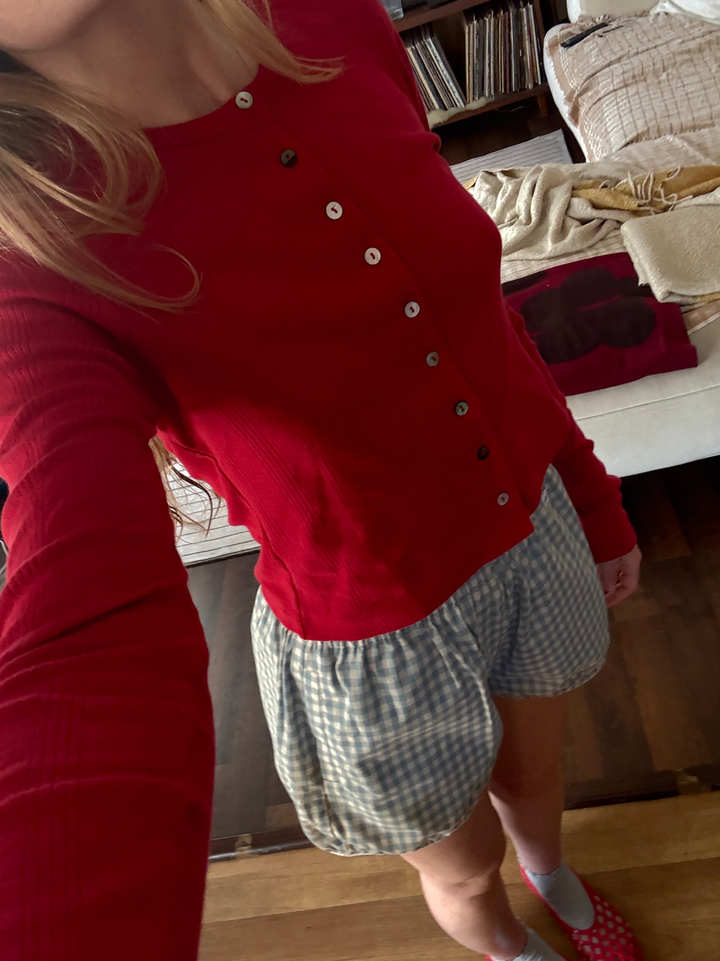 Red button-front cardigan with ribbed texture worn with blue gingham shorts in casual home setting
