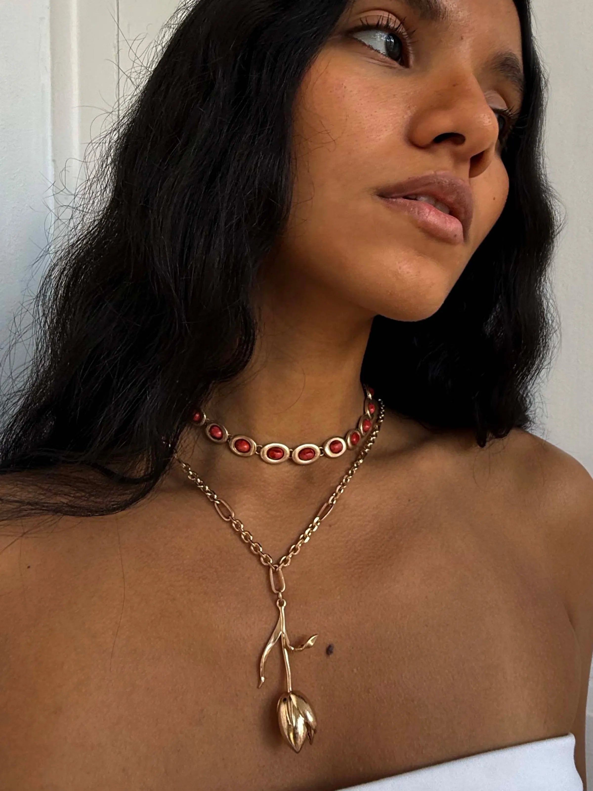Gold necklace with rose pendant and red gemstone choker layered on model's neck
