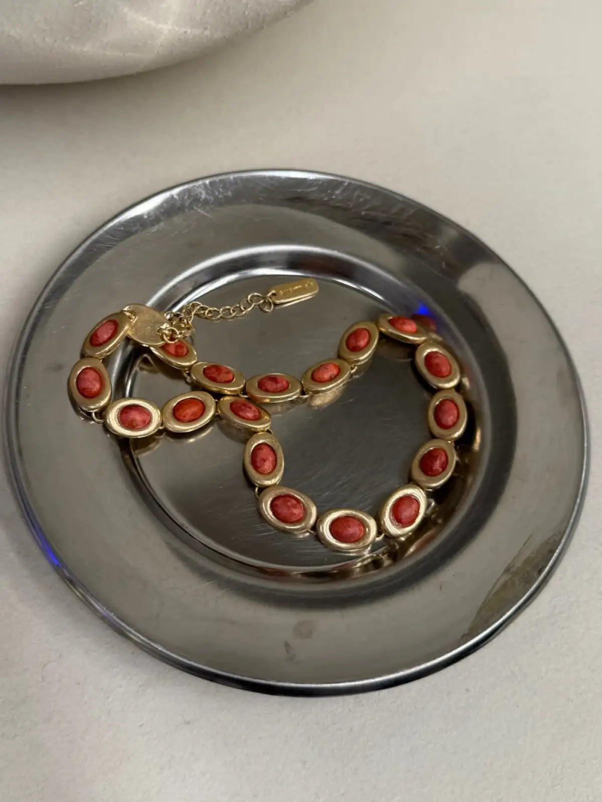 Gold-tone bracelet with oval red stones set in linked metal frames, displayed on silver plate