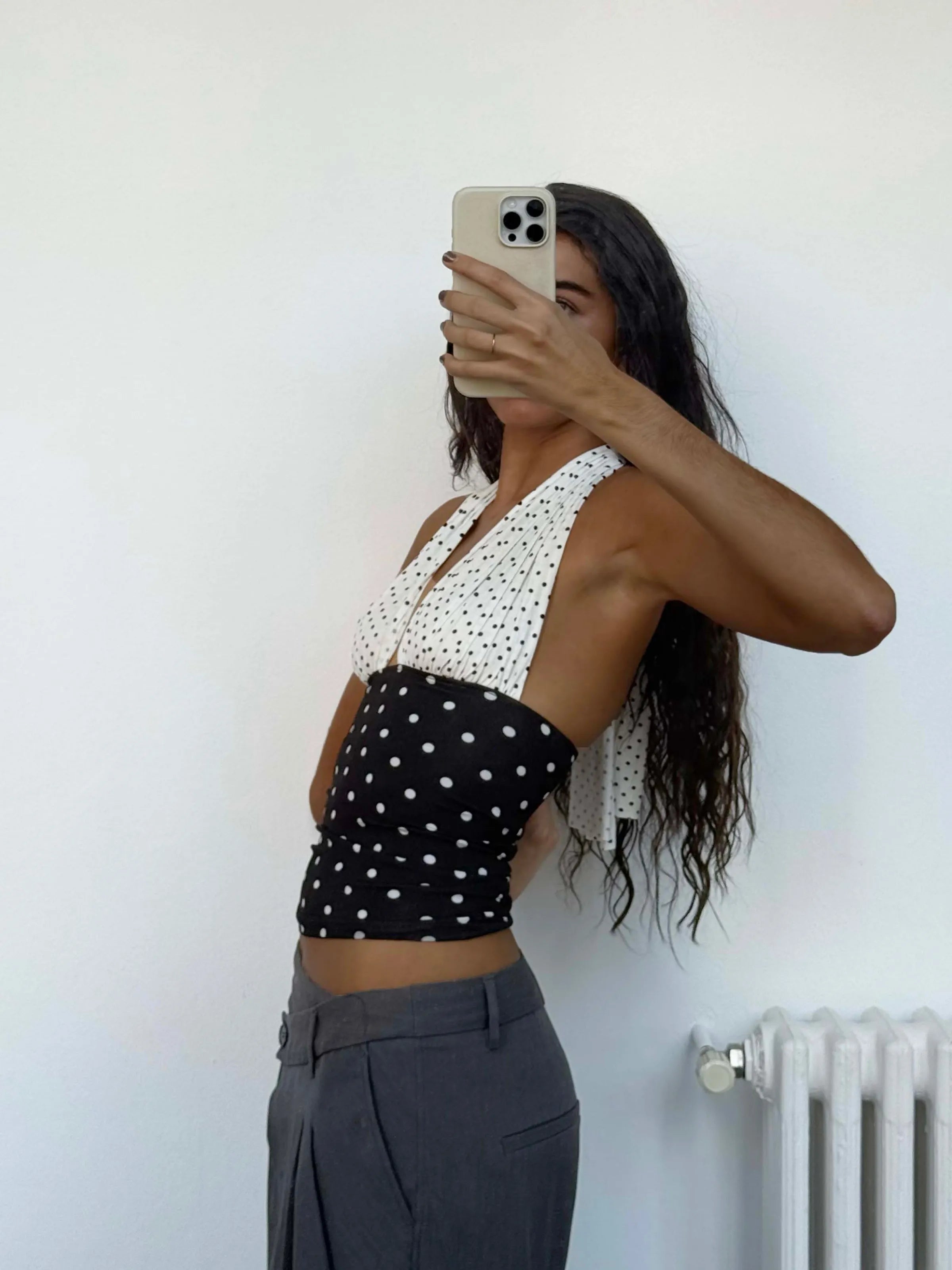 Woman wearing polka dot halter crop top with white top half and black bottom half, paired with gray trousers
