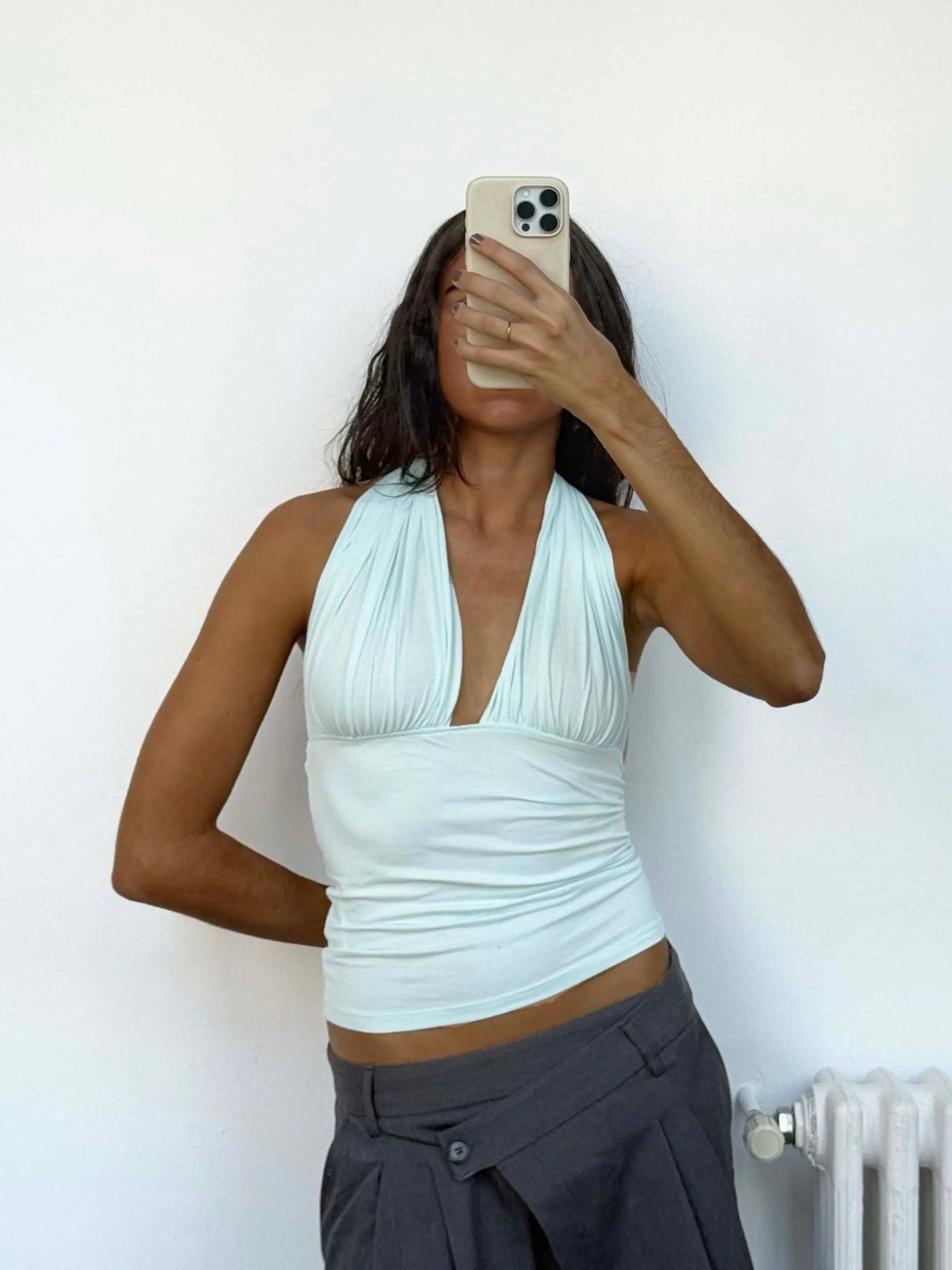 Mint green halter neck top with ruched V-neckline and fitted waist, worn with dark gray low-rise trousers