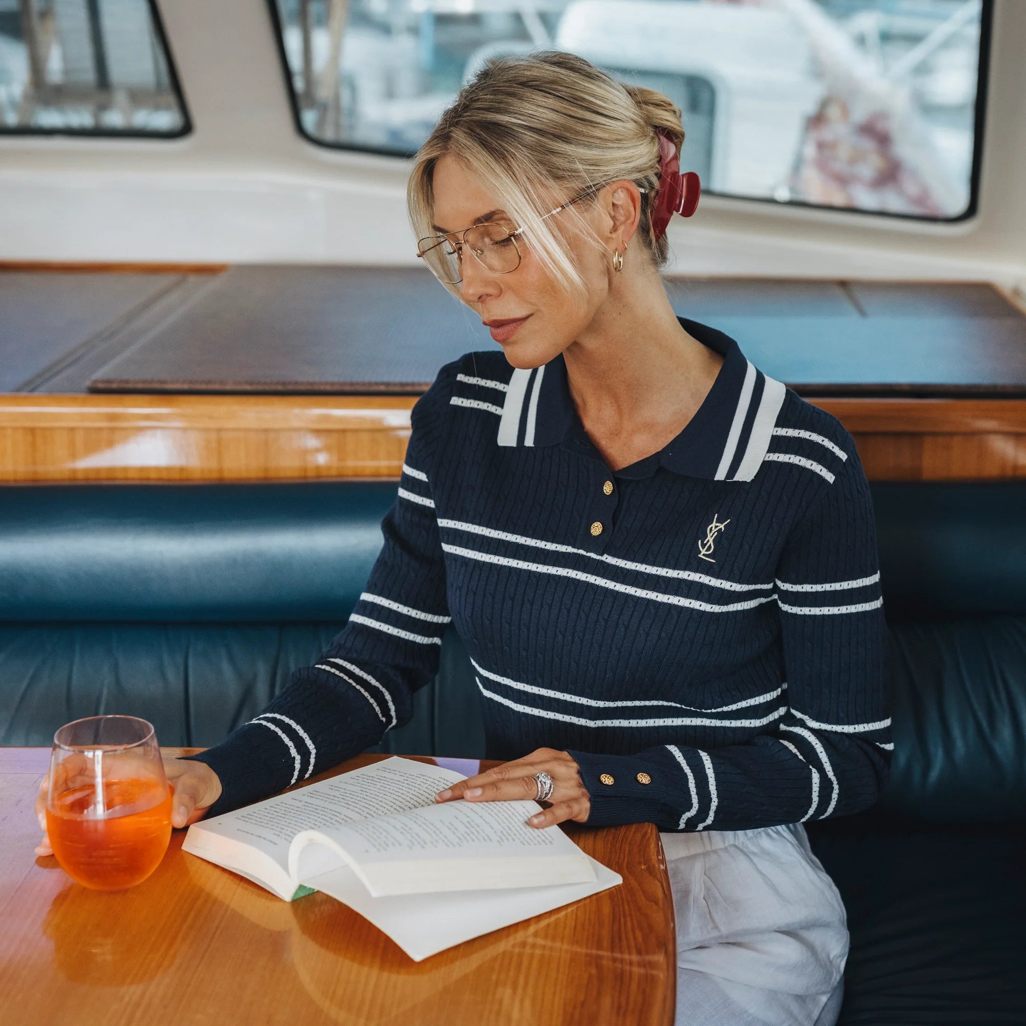 Woman reading a book on a boat with a drink beside her
