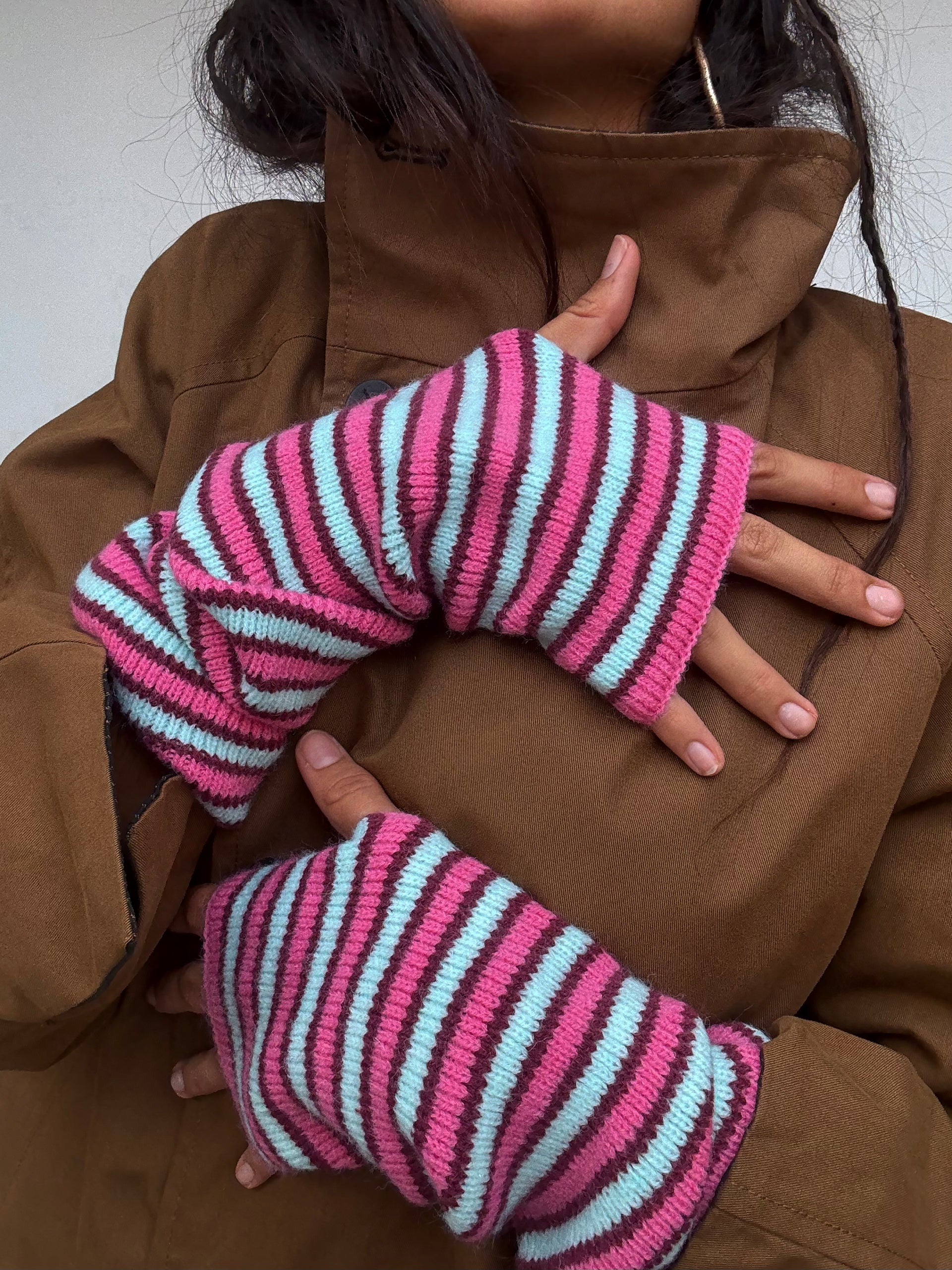 Striped fingerless gloves in pink, burgundy, and light blue knit fabric worn with brown hoodie