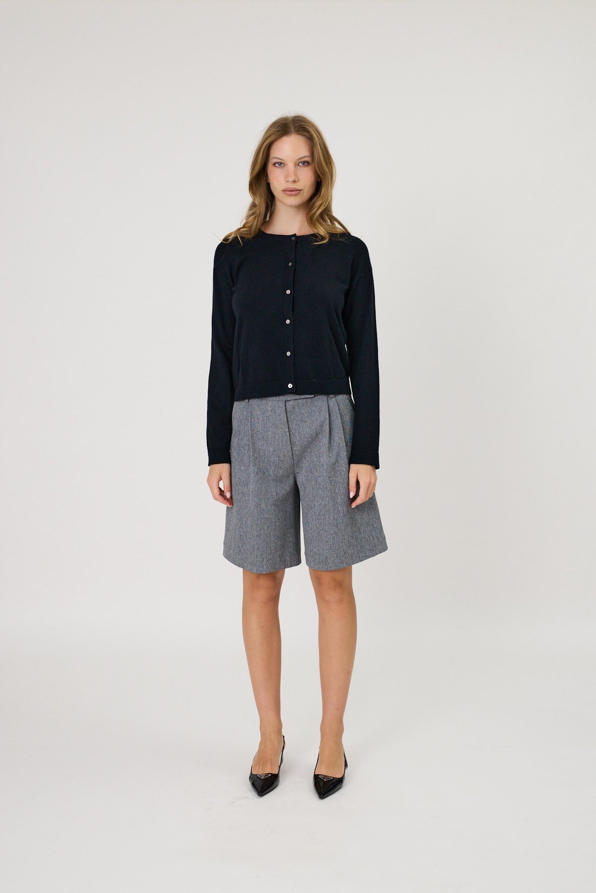 Navy blue button-front knit cardigan, long sleeves, round neck, lightweight fabric, worn with gray bermuda shorts.