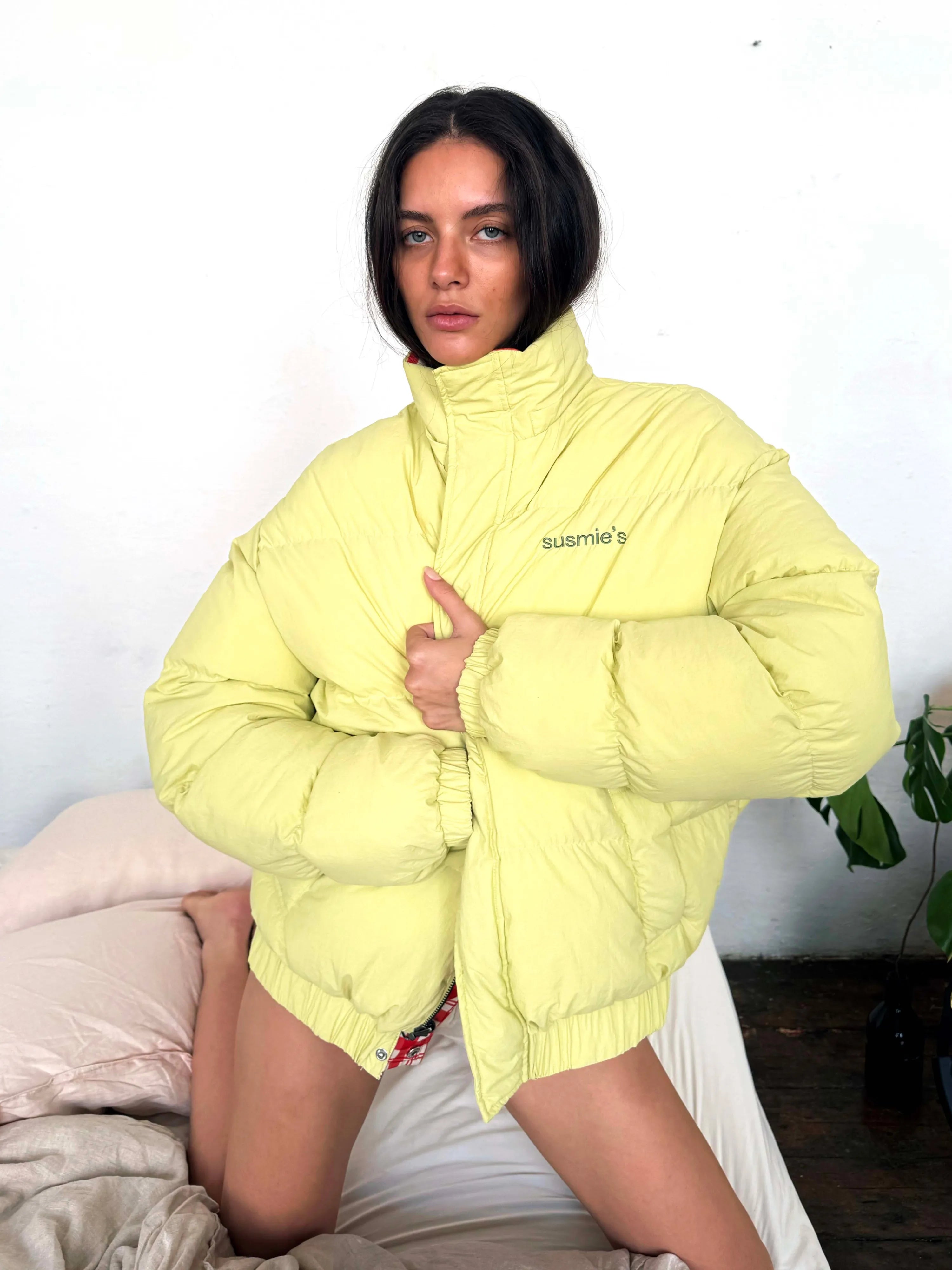 Yellow puffer jacket with high neck collar, quilted design, and susmie's branding on chest, shown on model