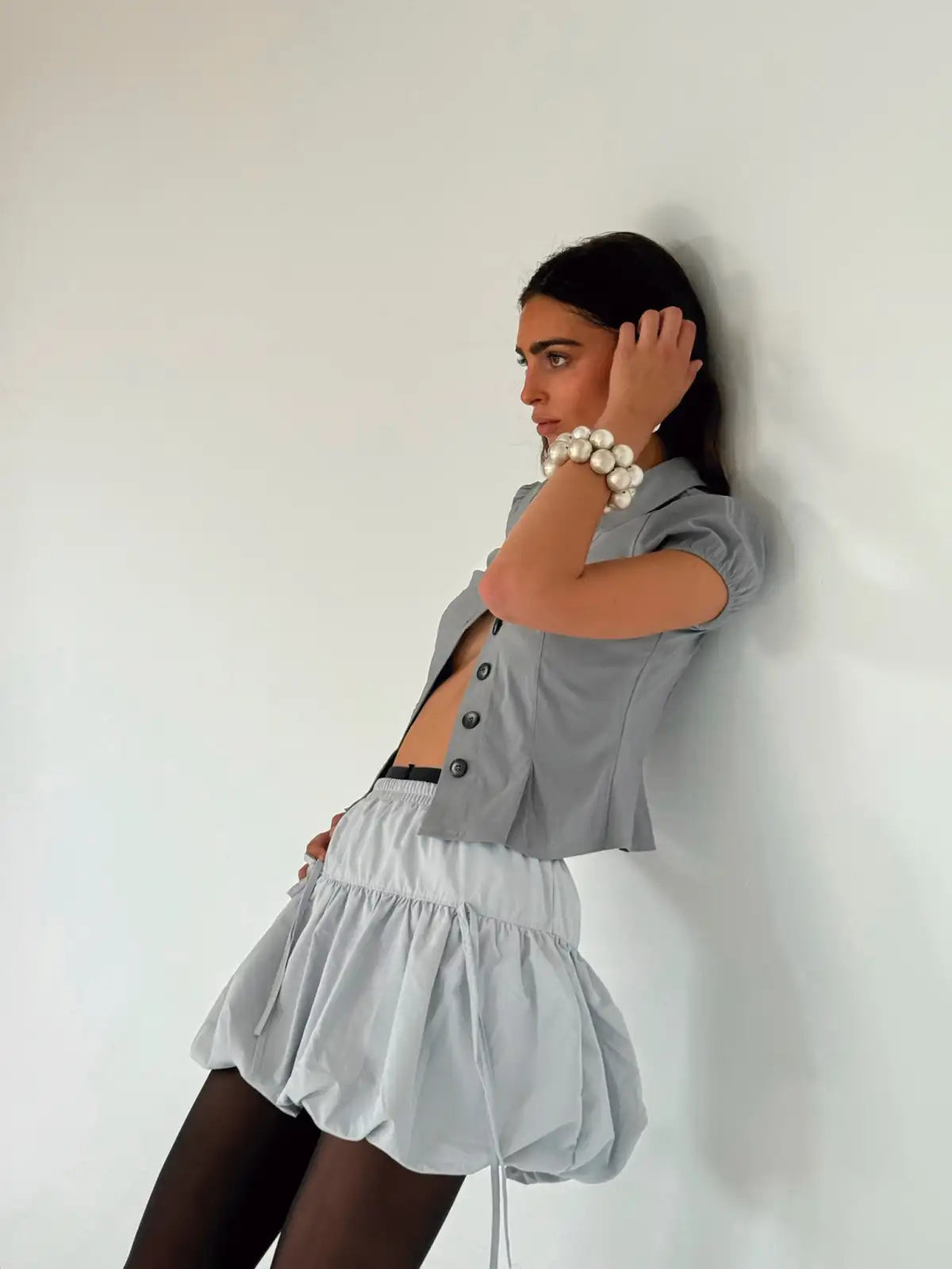 Gray short-sleeve cropped blazer with button front, paired with white tiered ruffle mini skirt and pearl bracelets
