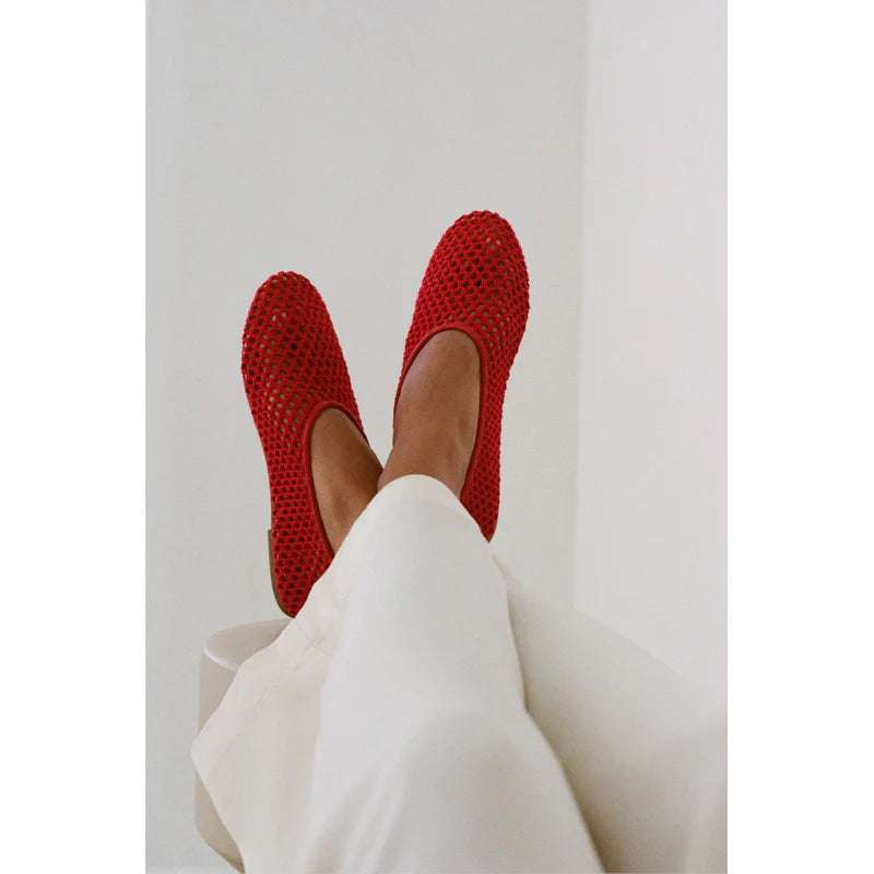 Red woven slip-on flats with textured mesh design, shown from above on person wearing white pants