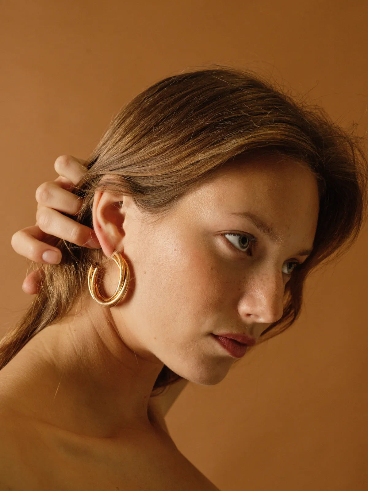 Gold chunky hoop earrings with smooth polished finish worn by model against warm beige background