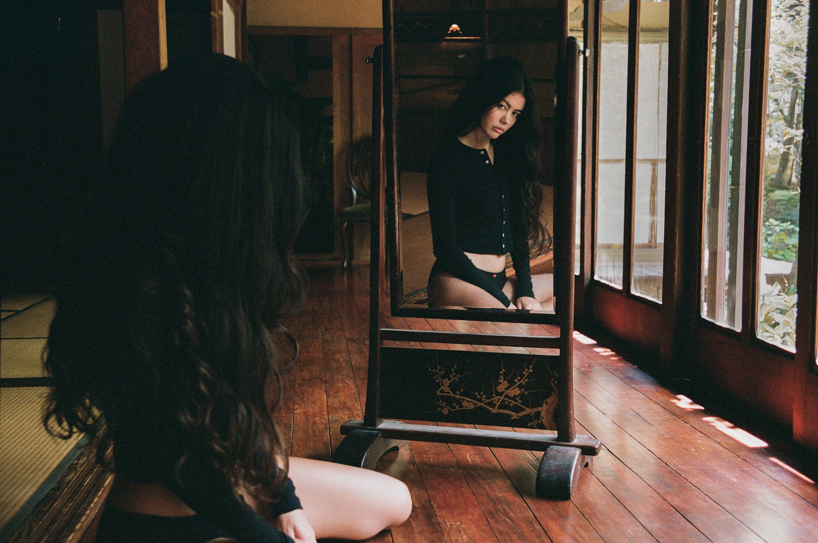 Woman in black outfit sitting in traditional Japanese room doorway with wooden floors and natural lighting