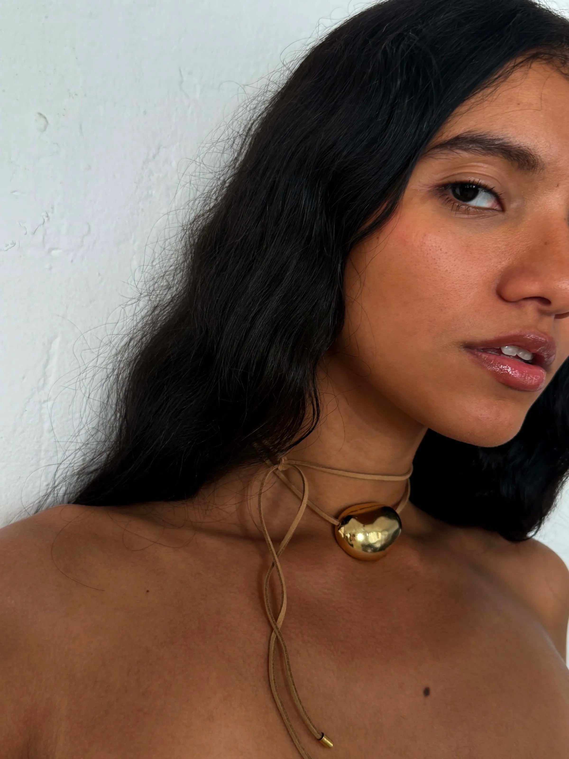 Gold sphere pendant on tan leather cord necklace with adjustable sliding closure worn by model with dark hair