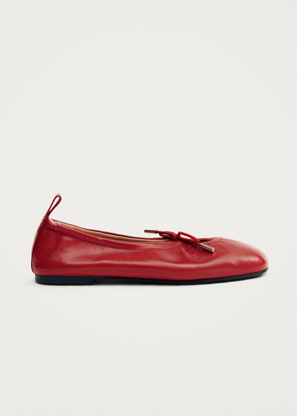 Red leather ballet flat with bow detail and gold metal tip accent, featuring a rounded toe and thin dark sole.