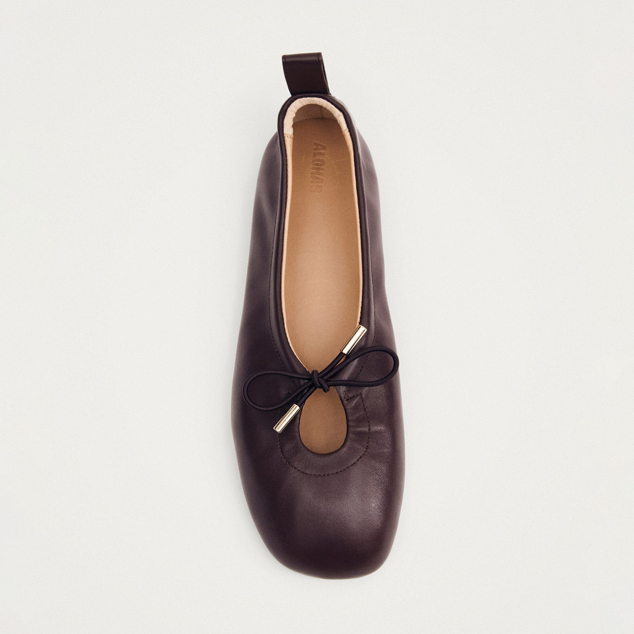 Dark brown leather ballet flat with bow detail and pull tab, viewed from above showing tan leather insole