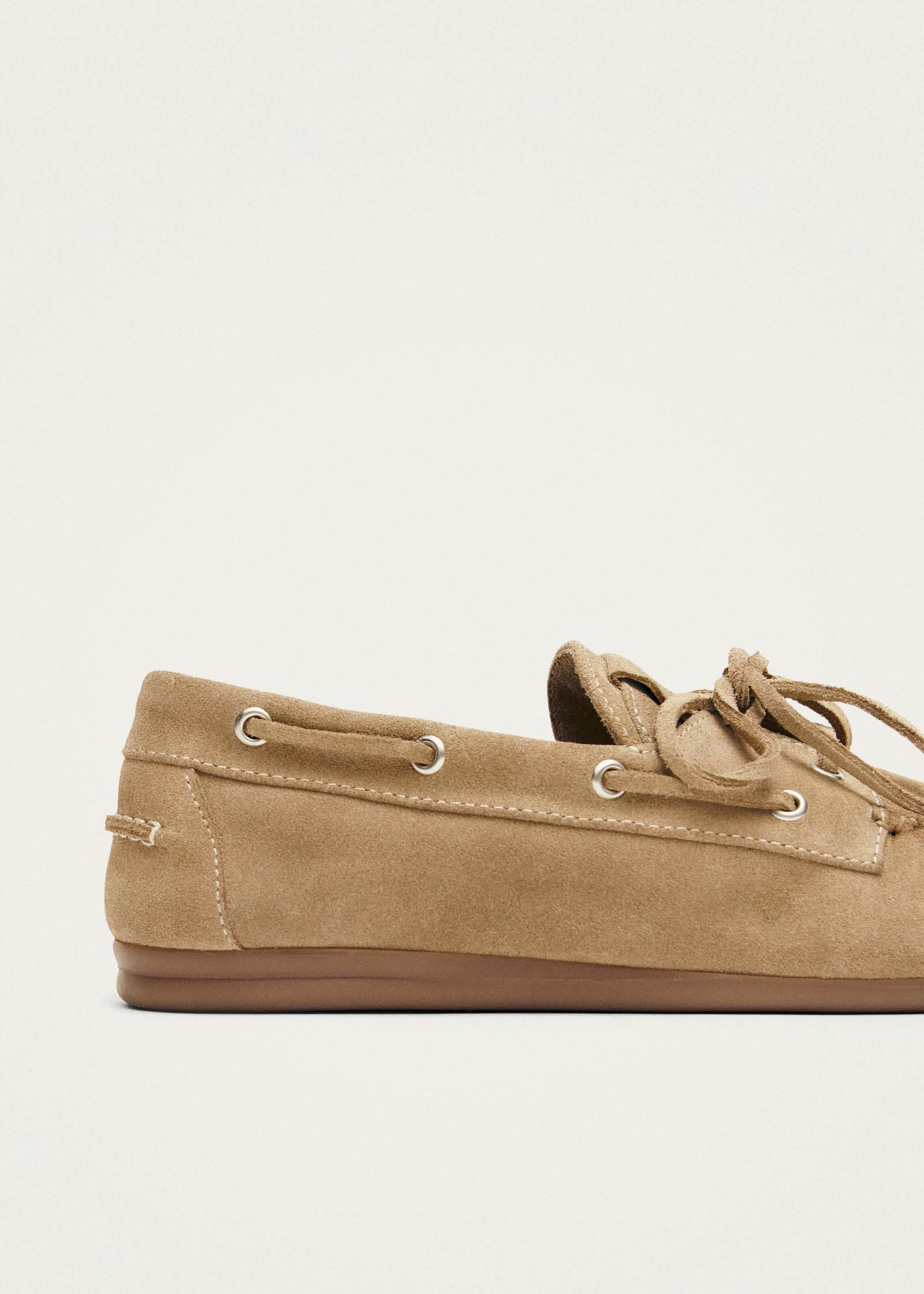 Tan suede boat shoes with laces and metal eyelets on white background