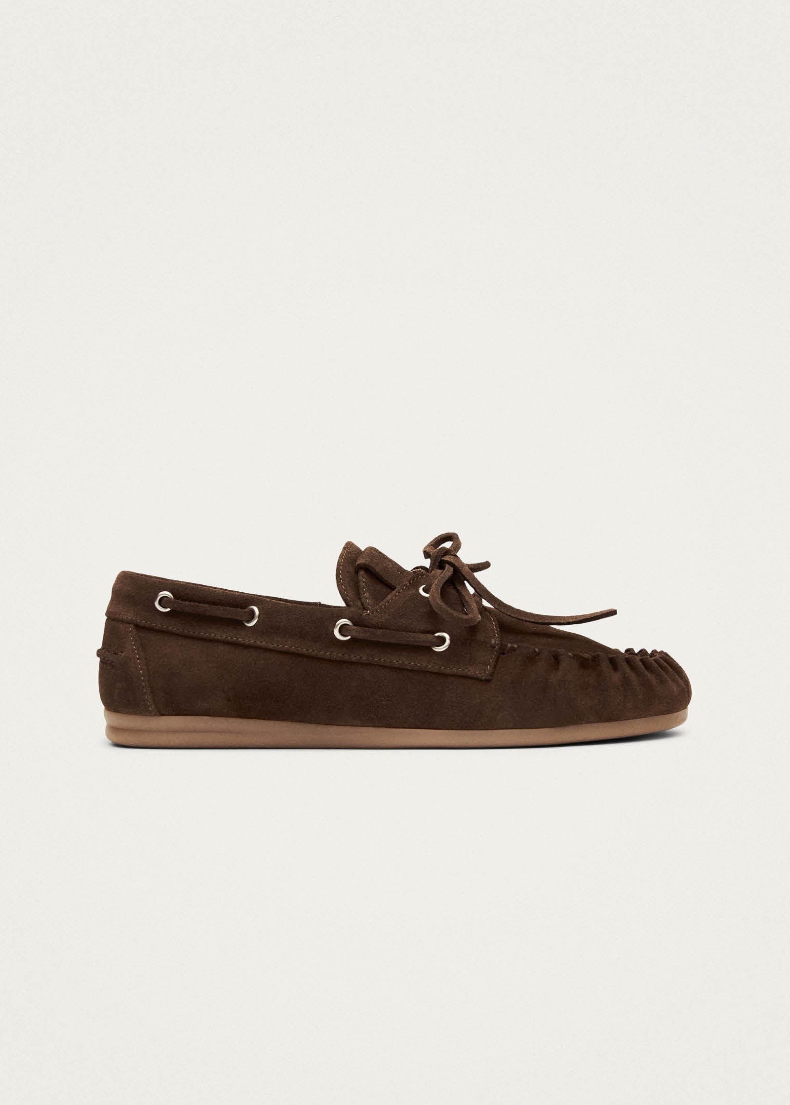 Brown suede moccasin slippers with lace-up detail and tan sole, displayed on side view against beige background