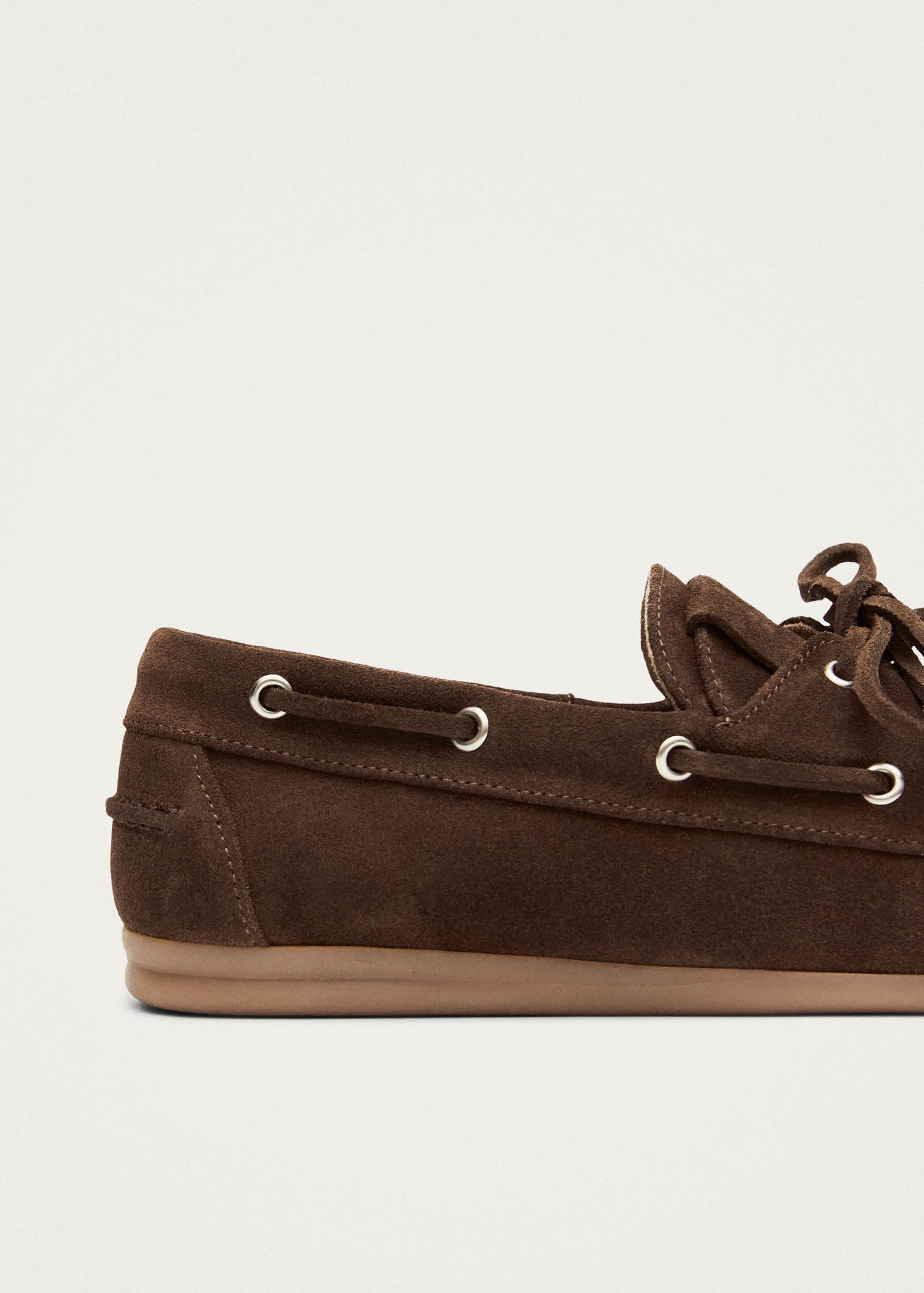 Brown suede boat shoe with leather laces and metal eyelets on beige sole, side profile view