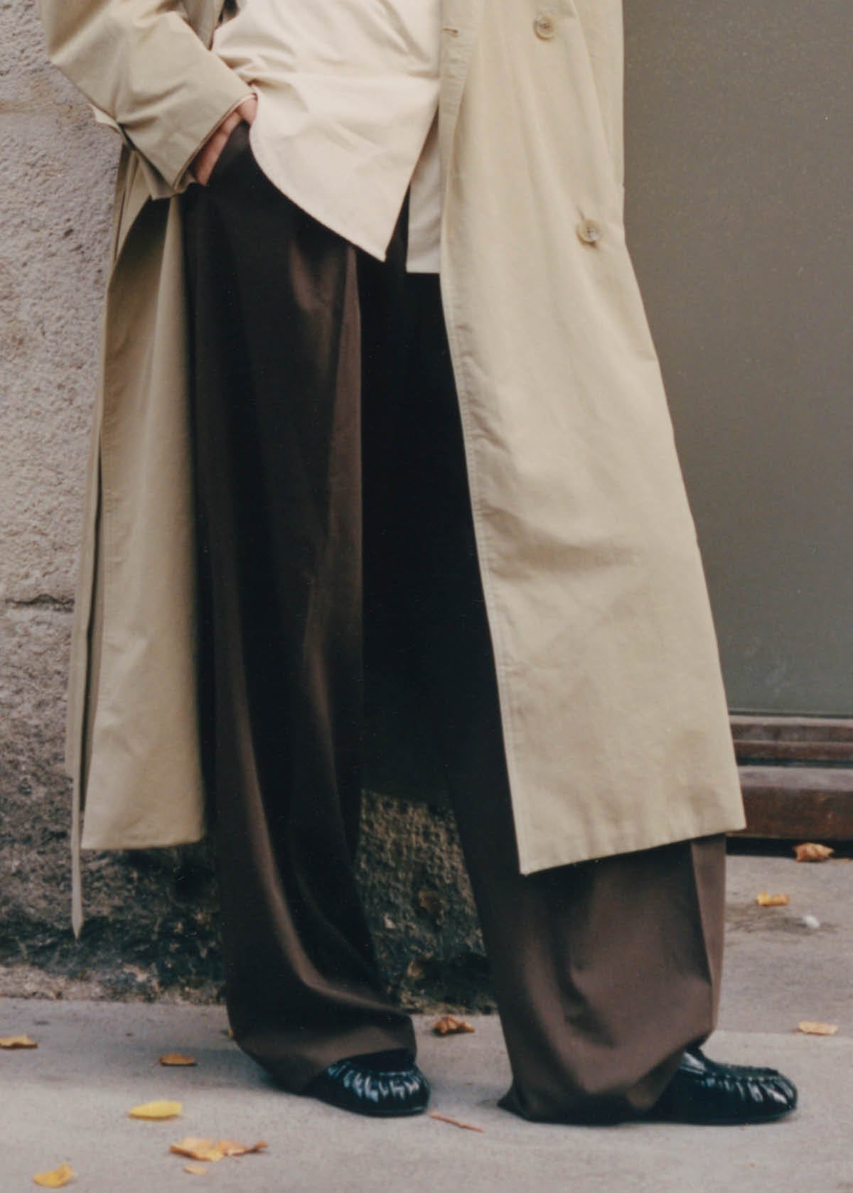 Person wearing black wide-leg pants with beige trench coat and black leather shoes on urban street