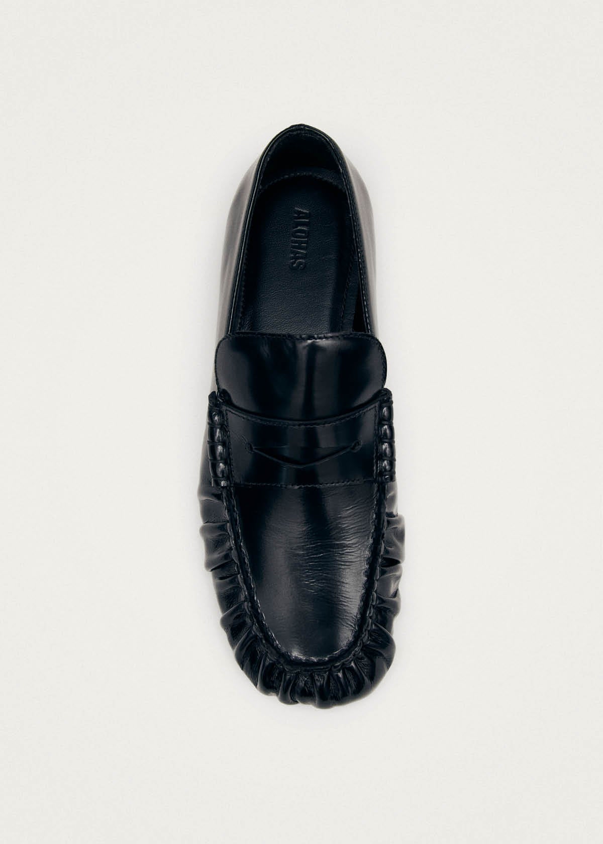 Black leather loafer with penny strap detail and moccasin stitching, viewed from above on light background