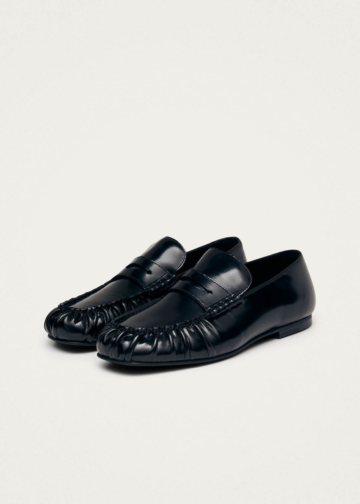 Black leather loafers with woven detail at toe and penny strap across vamp on beige background