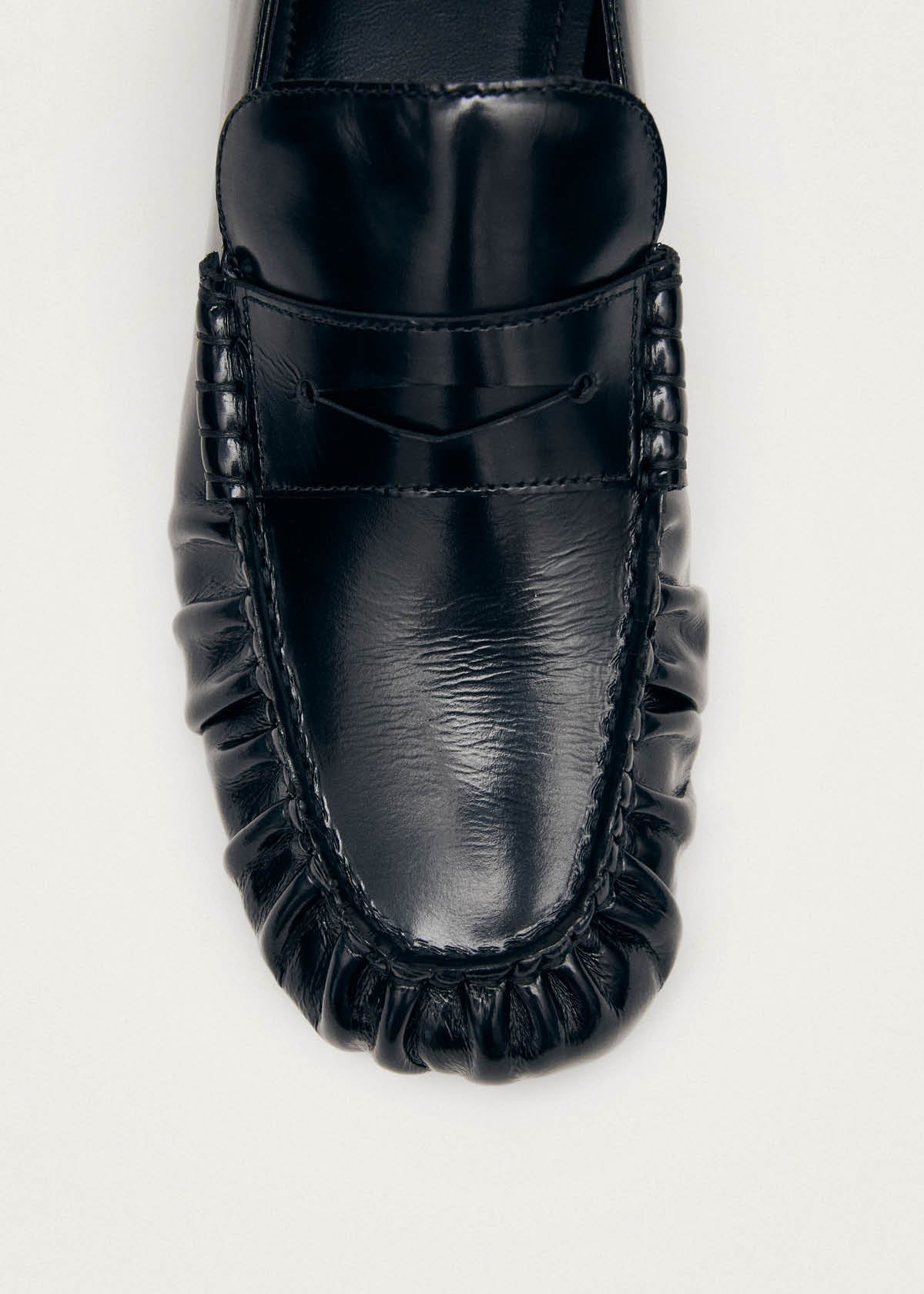 Black leather penny loafer with hand-stitched moccasin construction and woven detail around the sole
