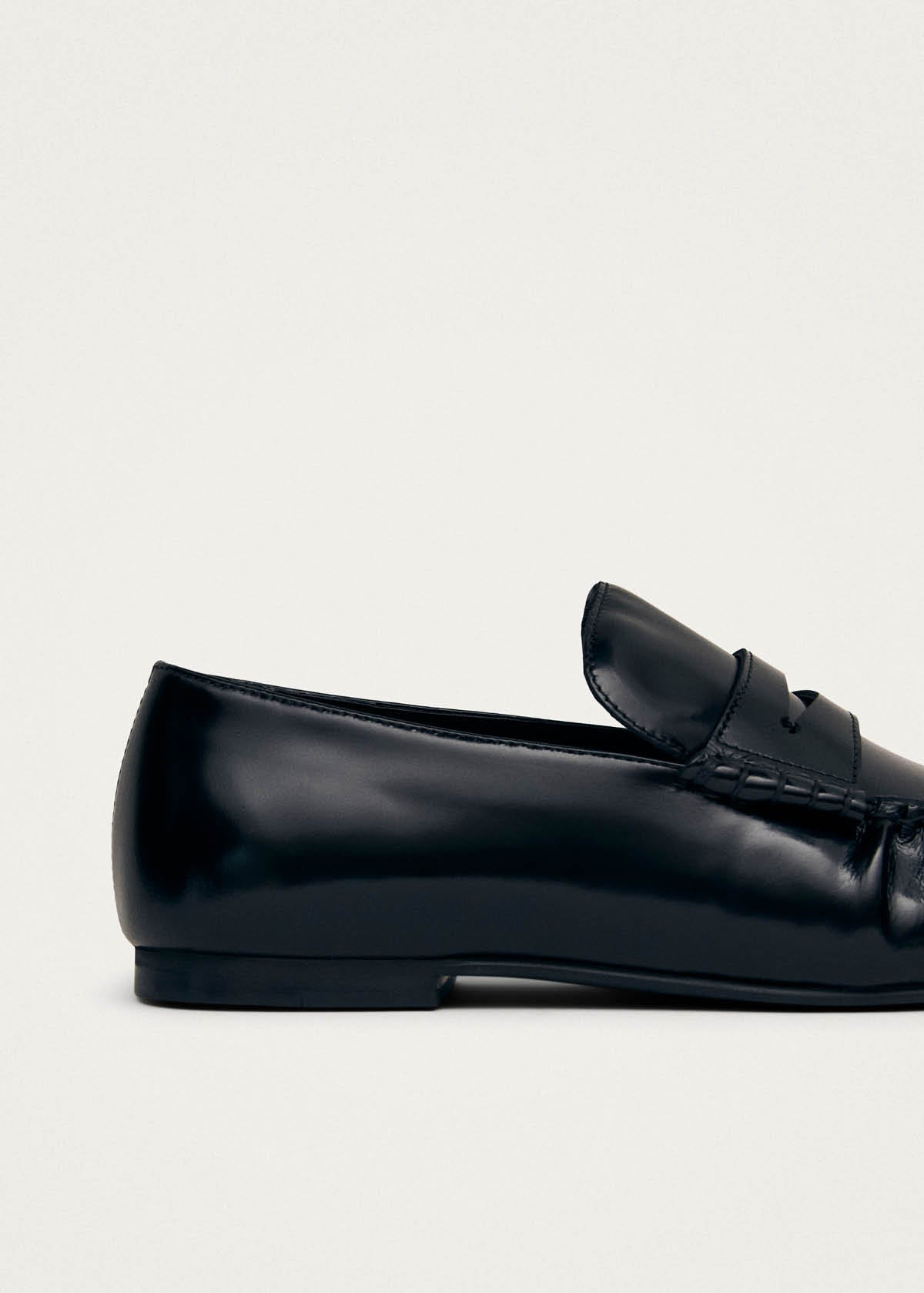 Black leather penny loafer shoes with stitched moccasin detail and low heel on neutral background