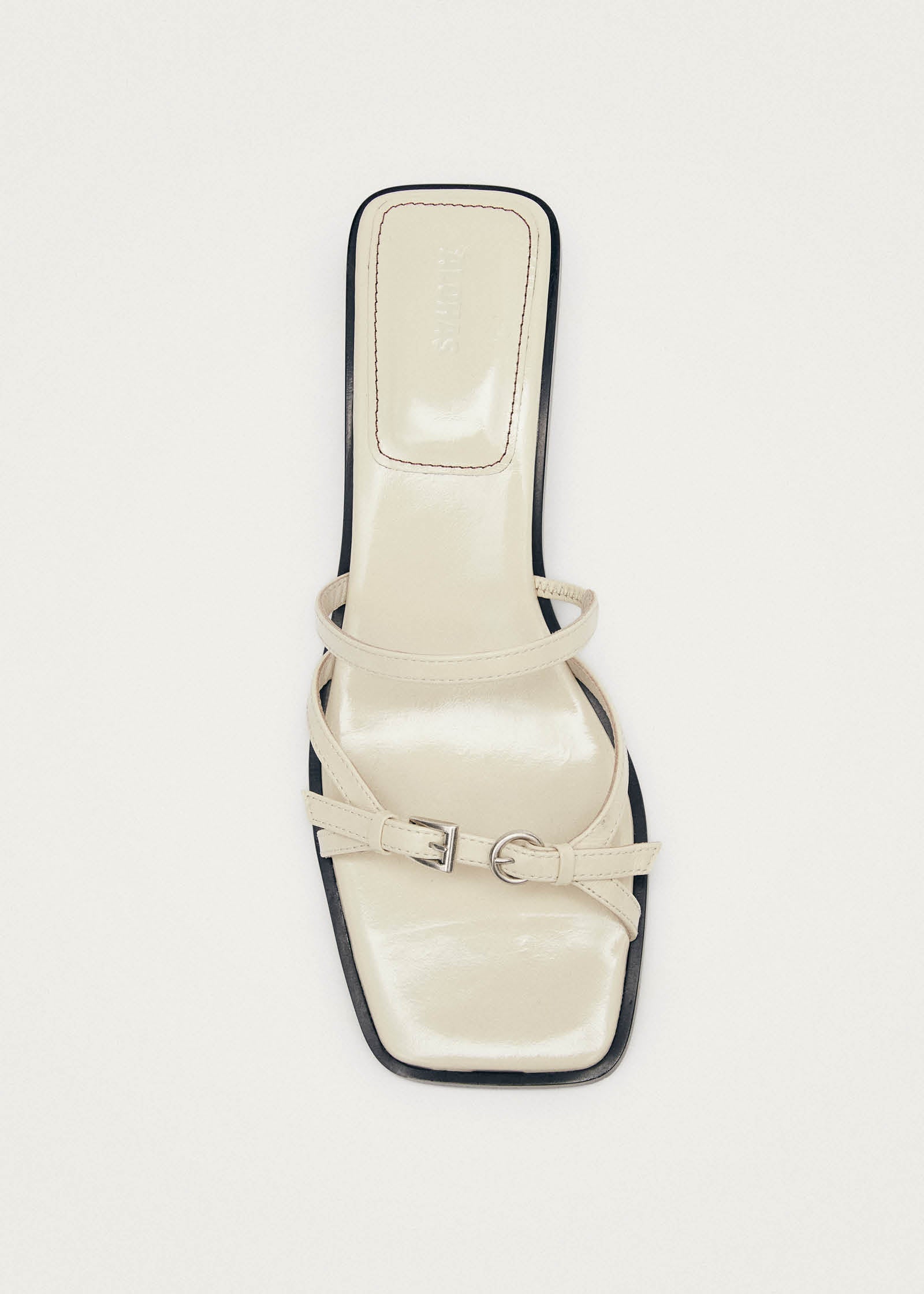 Cream leather square-toe sandal with dual buckle straps and black trim detailing, flat sole