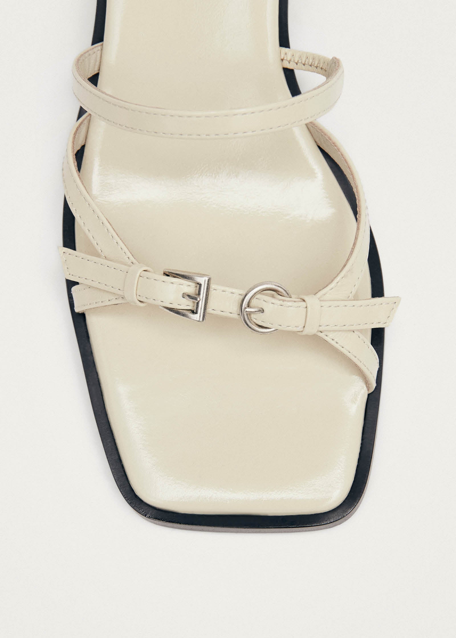 Cream leather strappy sandal with black sole and adjustable buckle details across the toe and ankle