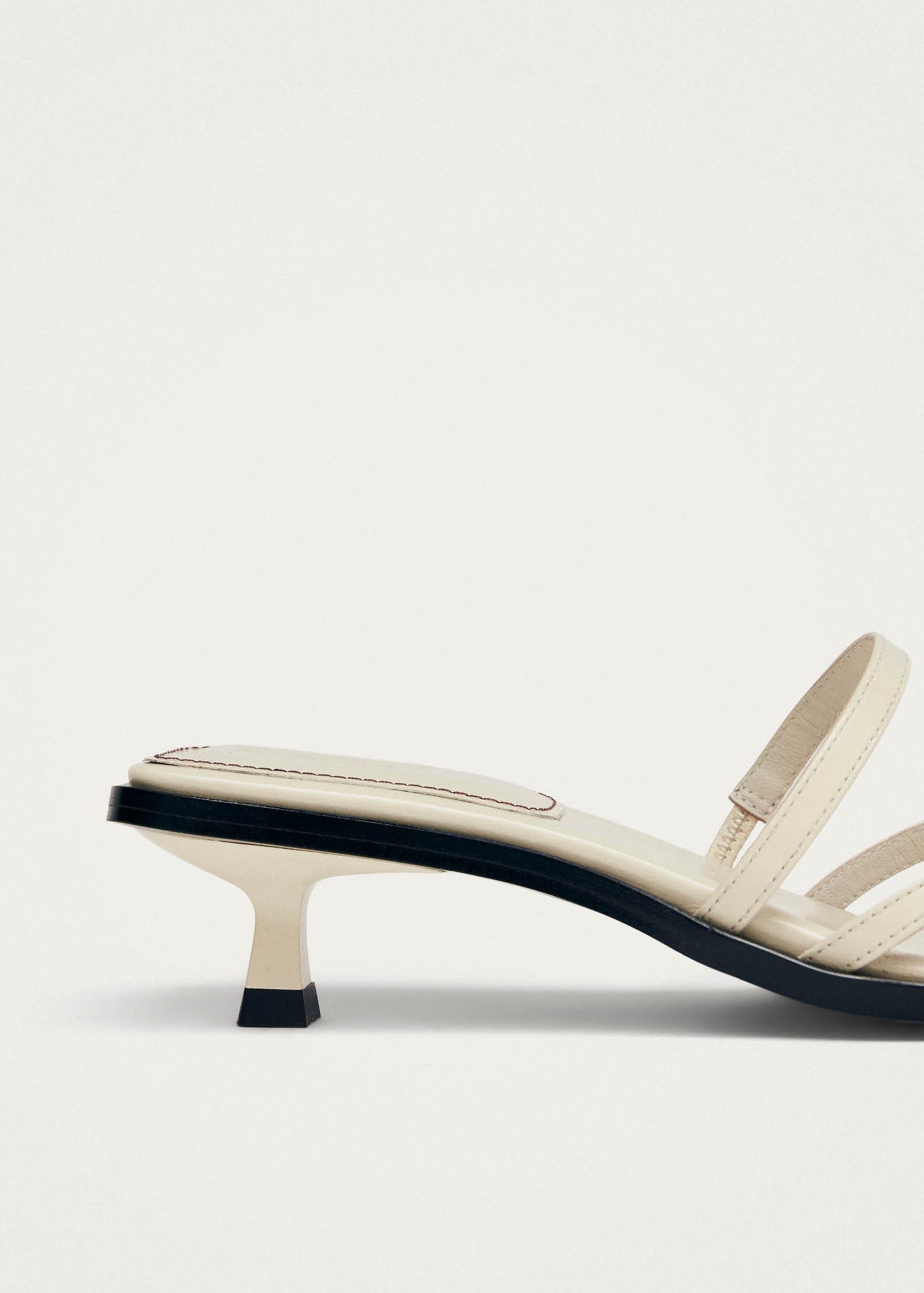 Cream leather kitten heel mule sandal with black sole and slingback strap on beige background