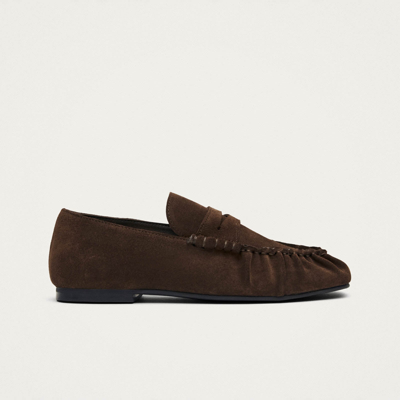 Brown suede penny loafer with moccasin stitching and black sole, shown in side profile view