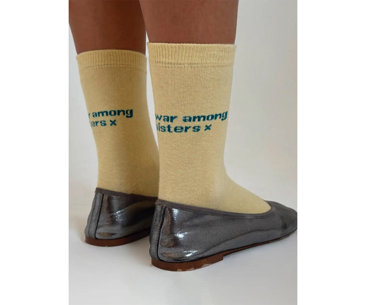Pale yellow ribbed socks with blue text reading "war among sisters" worn with black leather flats