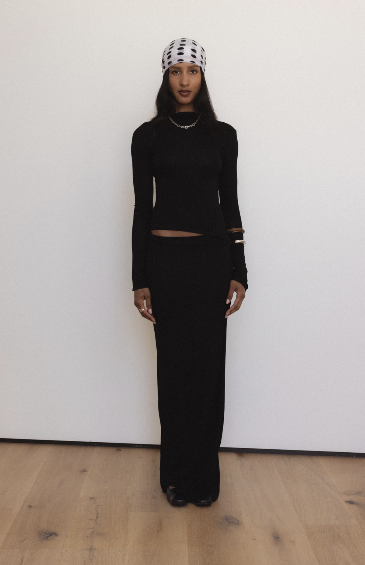 Woman wearing black long-sleeve crop top and maxi skirt set with polka dot beanie and silver chain necklace