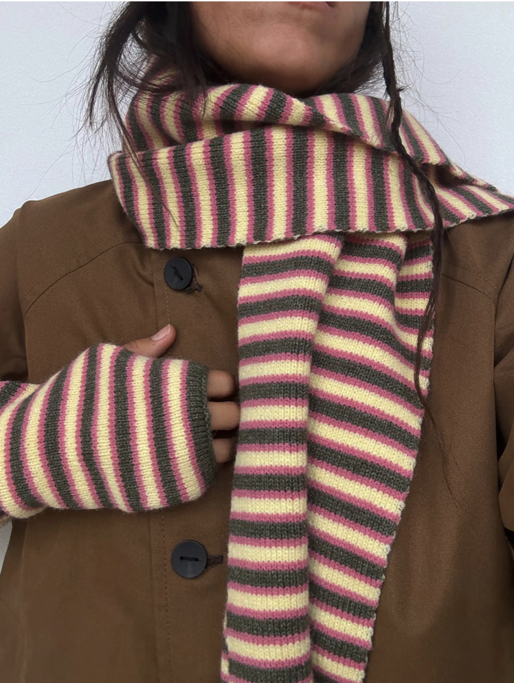 Striped knit scarf and fingerless gloves set in pink, cream, and gray worn with brown coat